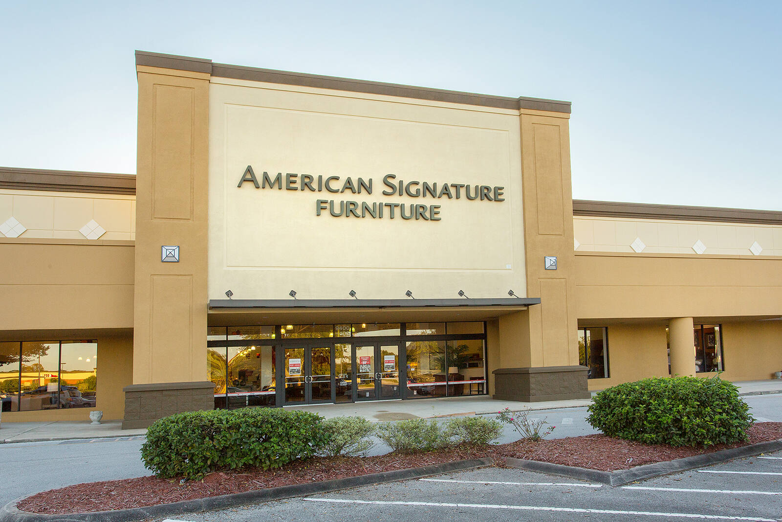 Short green shrubs in front of American Signature Furniture on a clear day