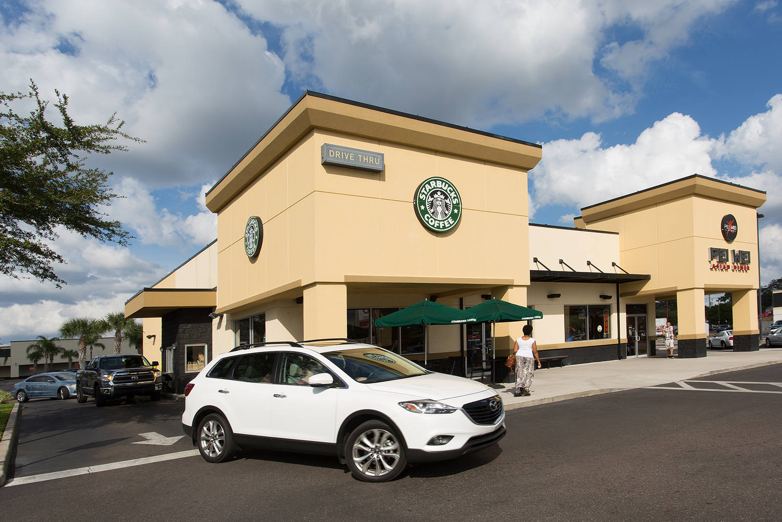 White SUV turning past Starbucks coffee shop with a cloudy blue sky.