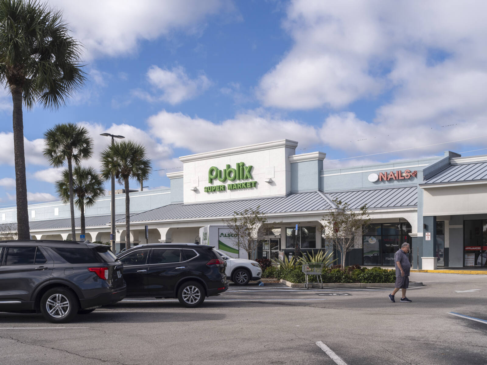 Busy parking lot and patron walking towards entrance of Publix supermarket.
