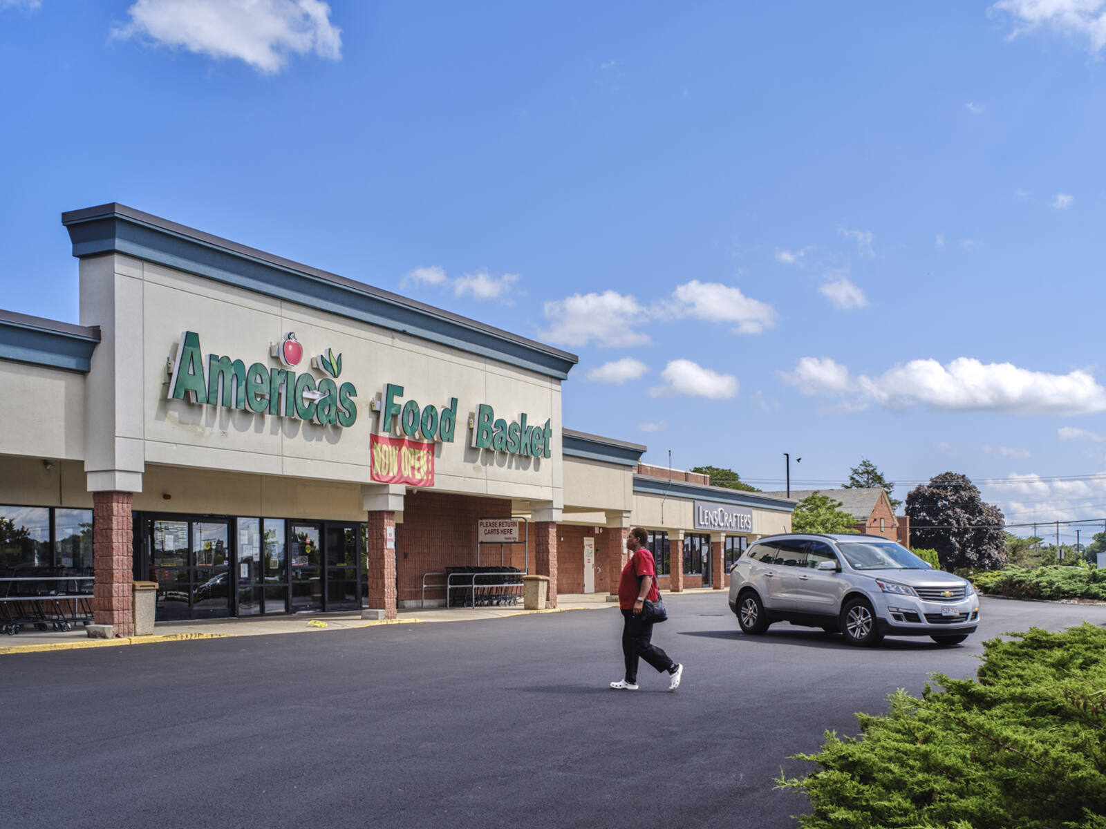Pedestrian and Grey SUV pull up to America's Food Basket grocery store.