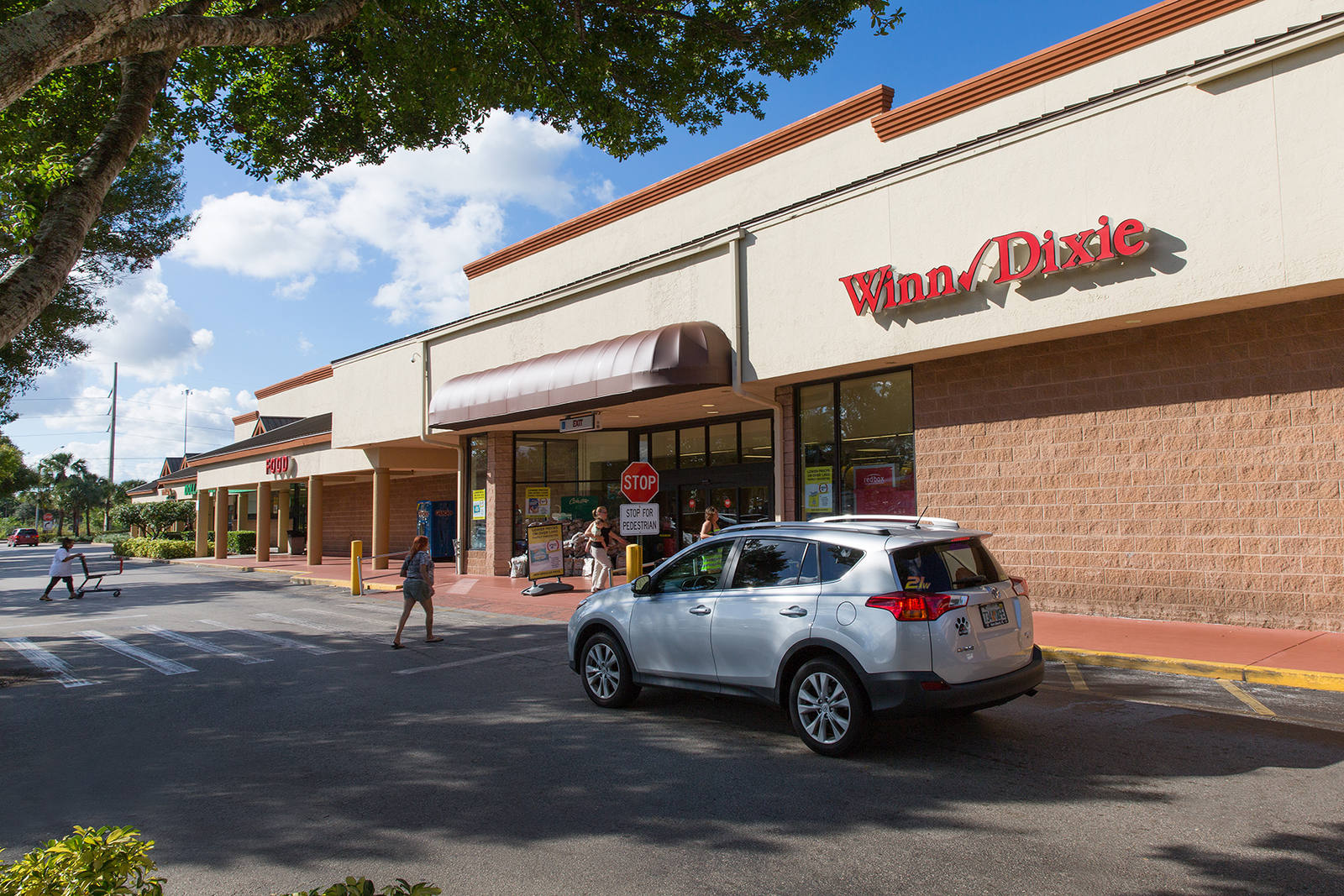 Person walking in front of white car at Winn Dixie at Shoppes of Victoria Square