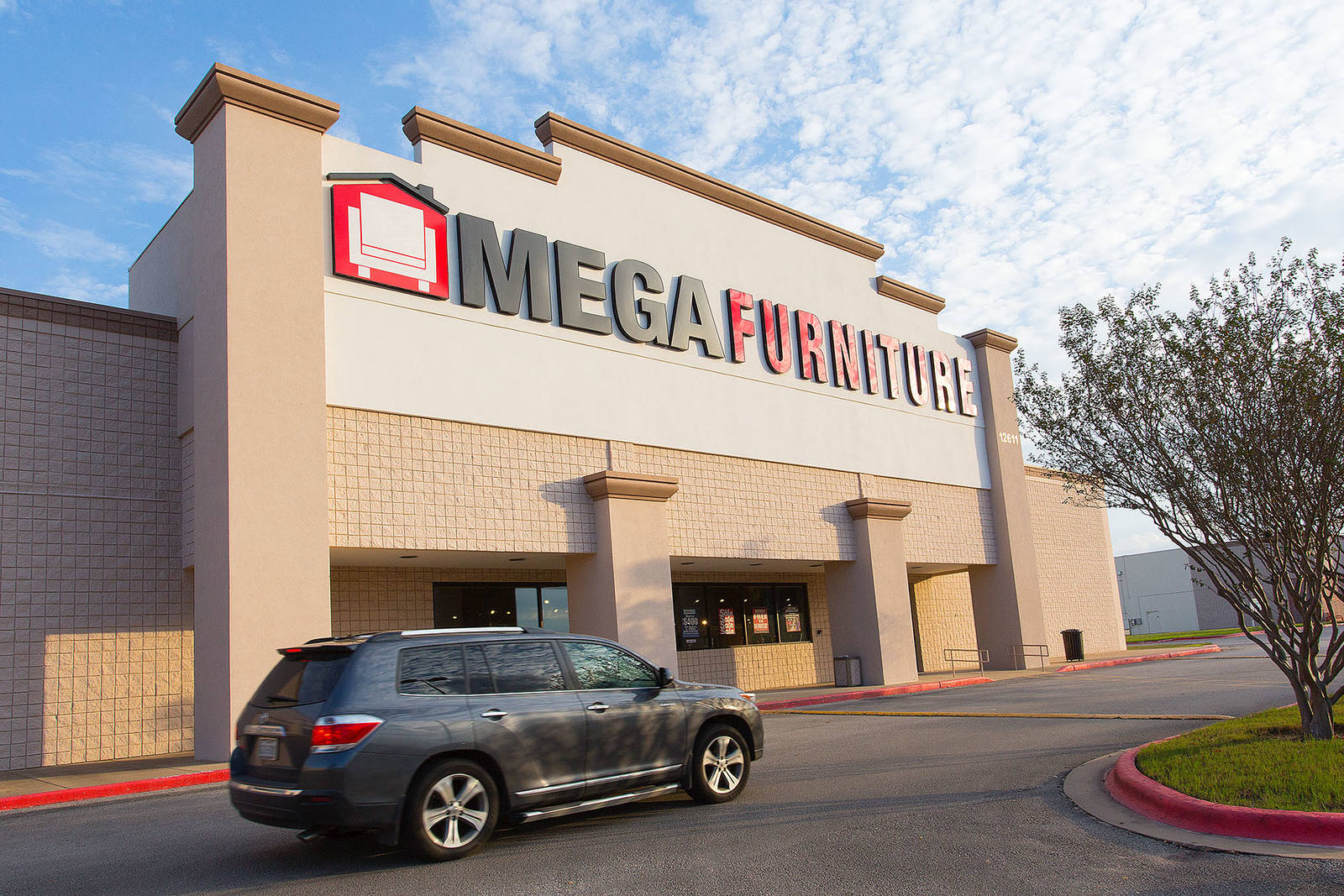 Dark grey SUV passing entrance of Mega Furniture at Parmer Crossing Shopping Center
