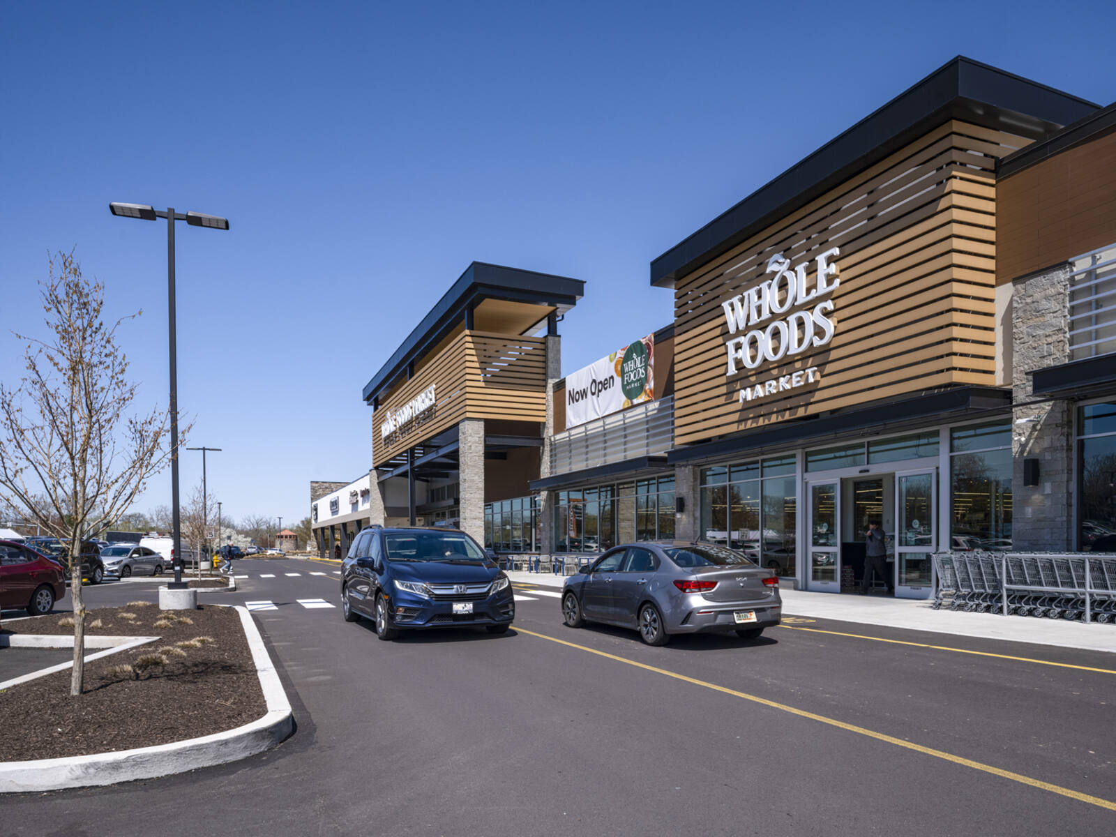 Cars pass Whole Foods Market on access road at shopping center.