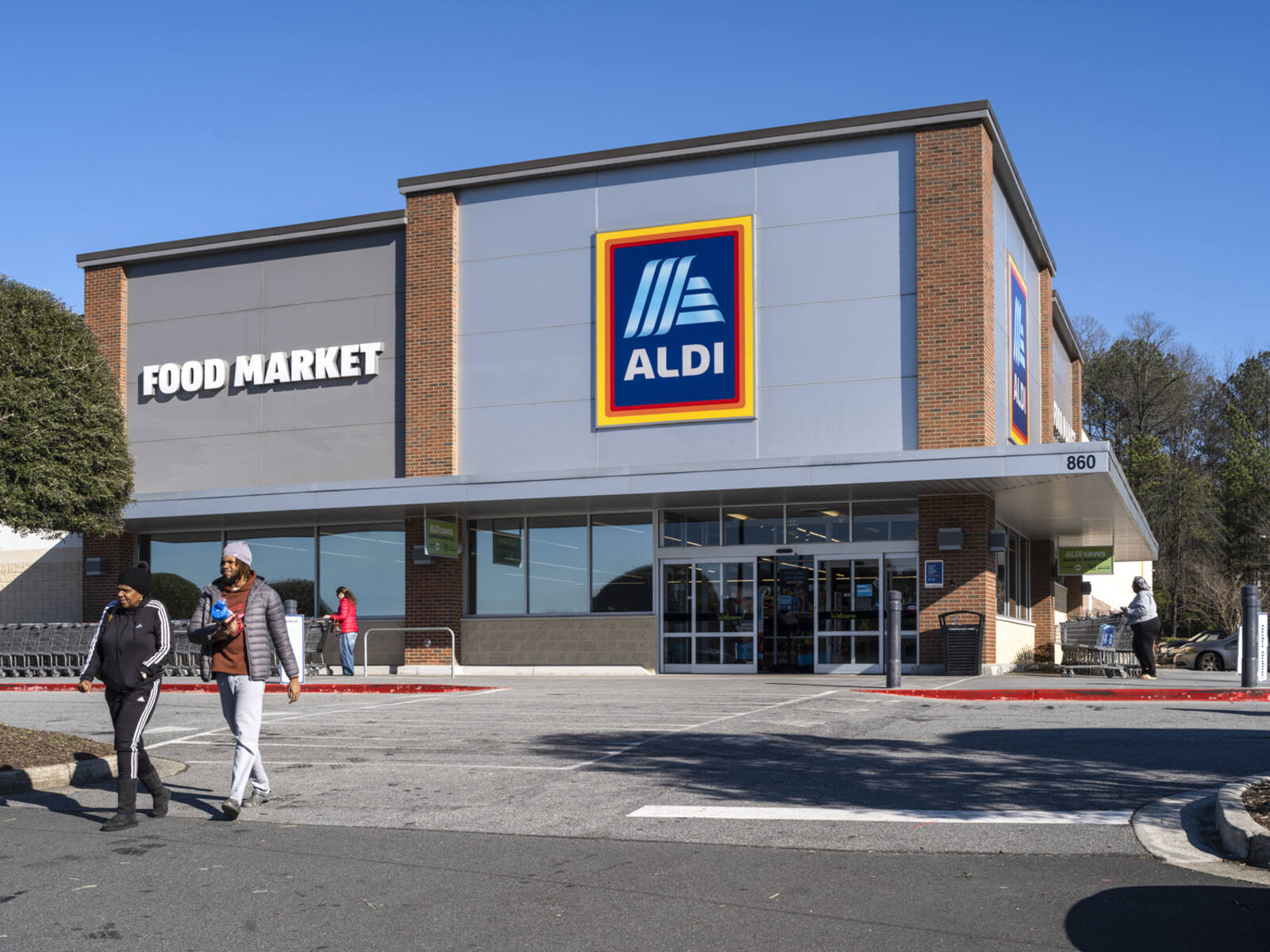 Two patrons leaving Aldi with trees behind store.