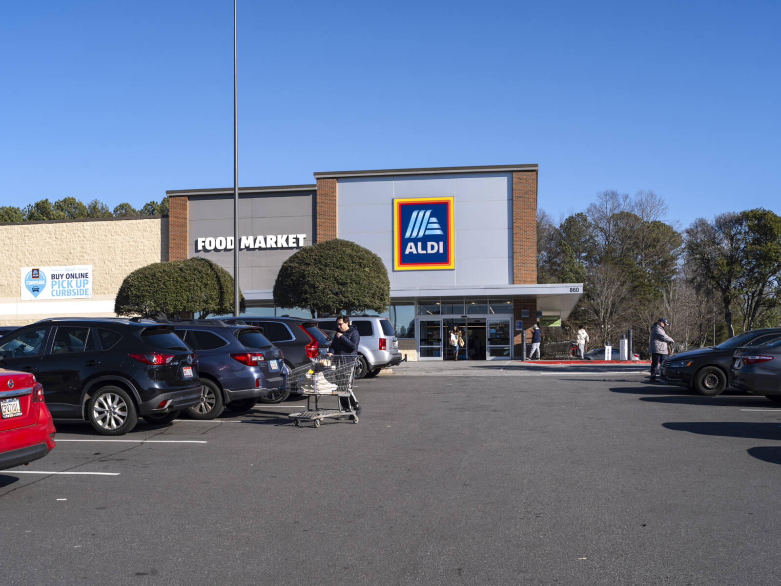 Busy parking lot and patron with shopping cart in front of Aldi.