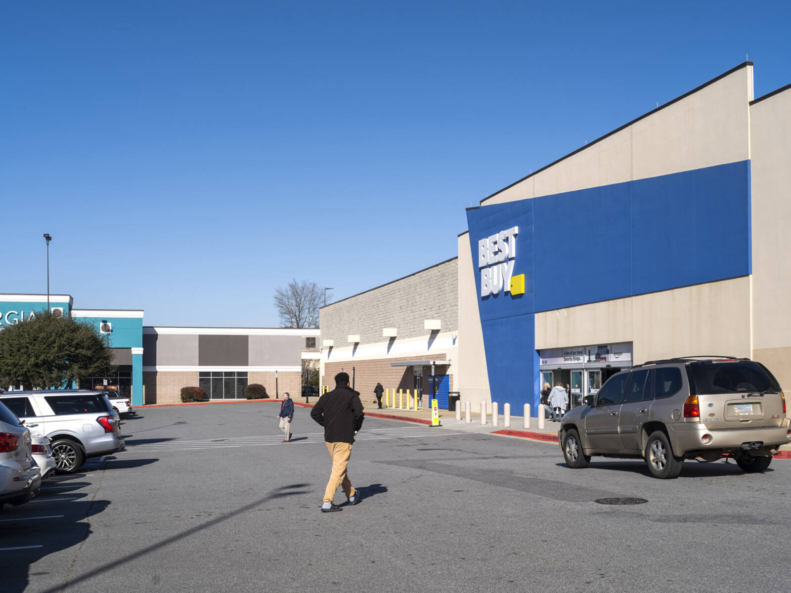 Man approaches Best Buy with SUV pulled over at entrance.