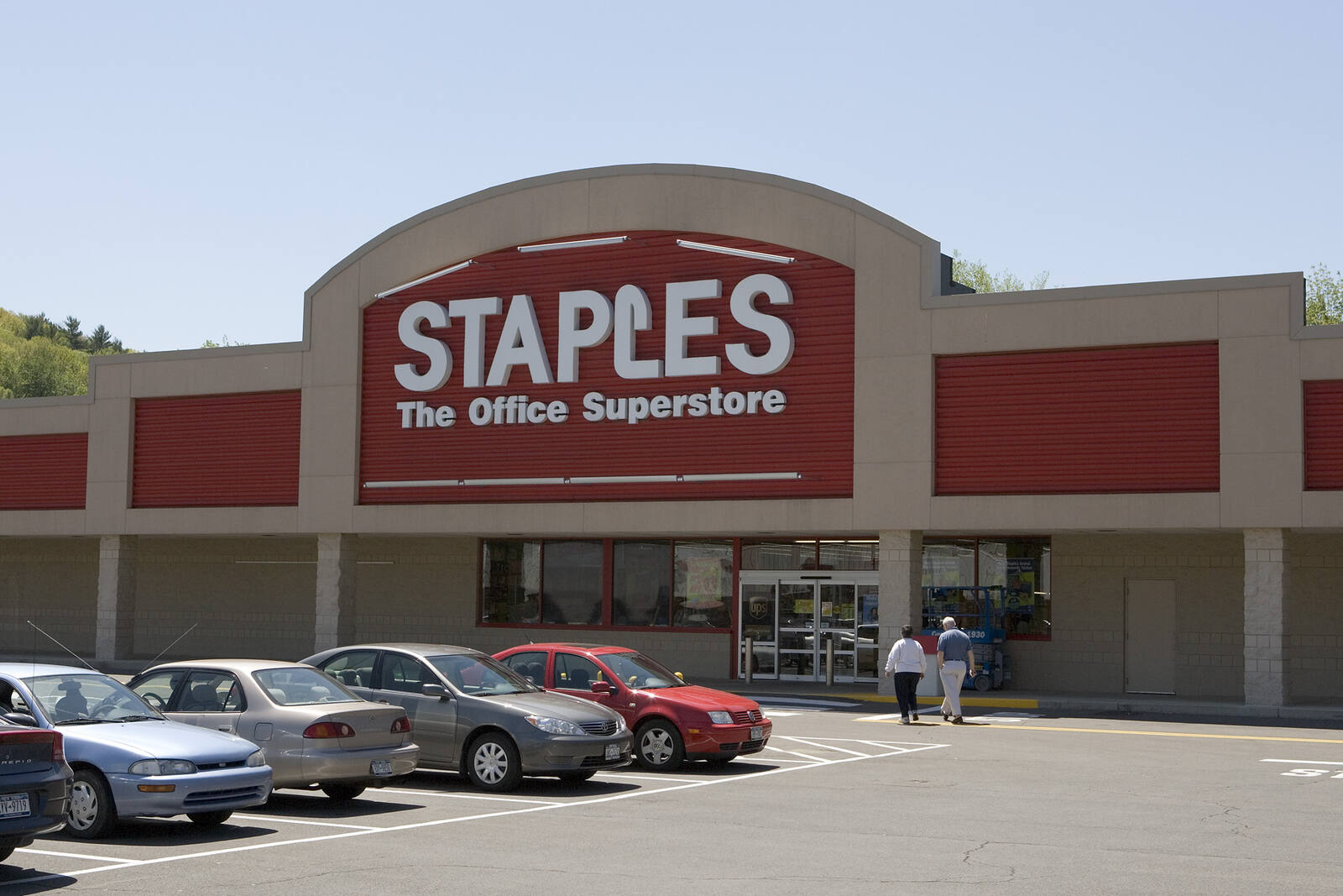 A couple walks past row of parked cars to enter Staples at Campus Plaza.