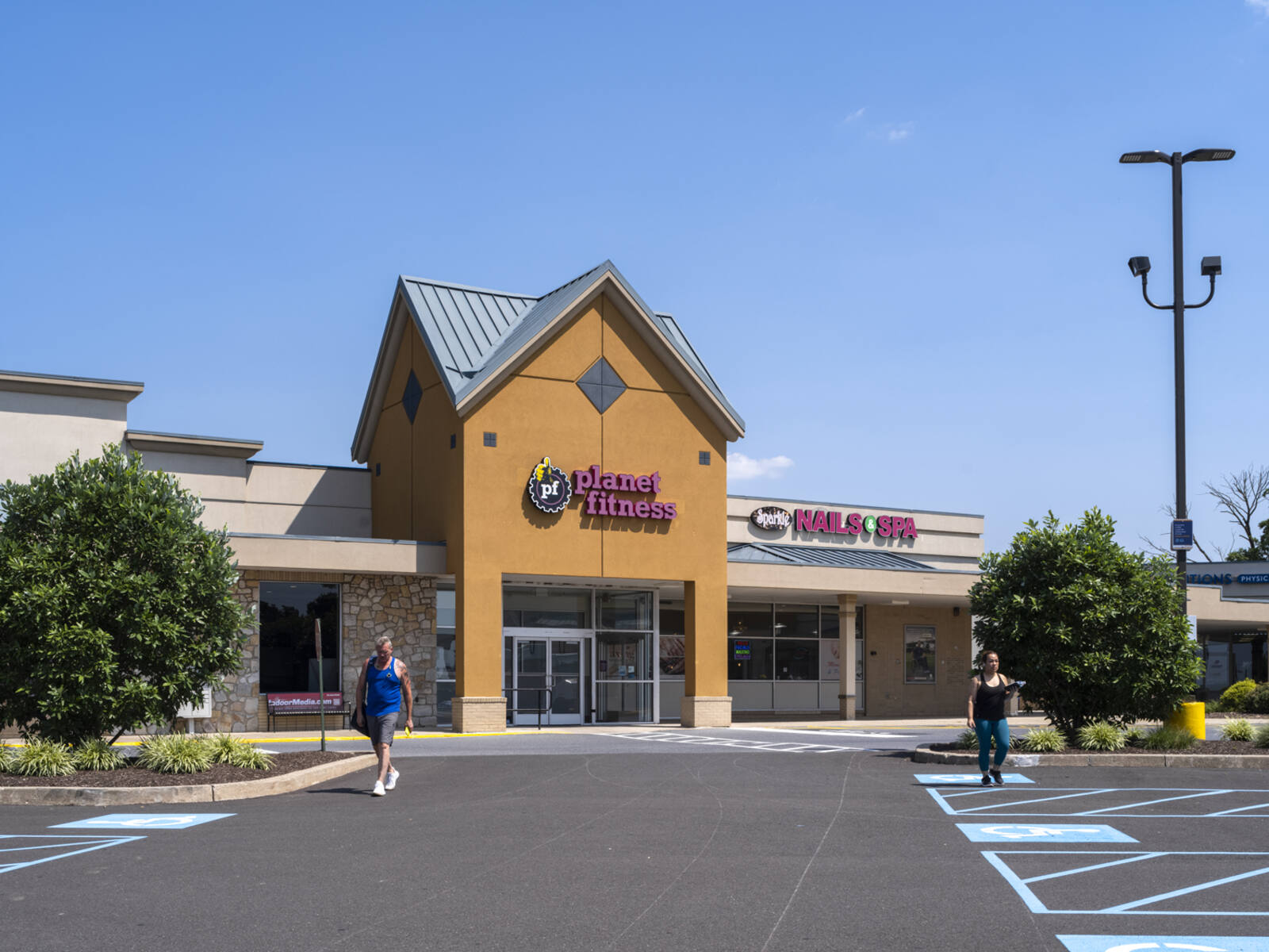 Two patrons exit Planet Fitness gym into parking lot.