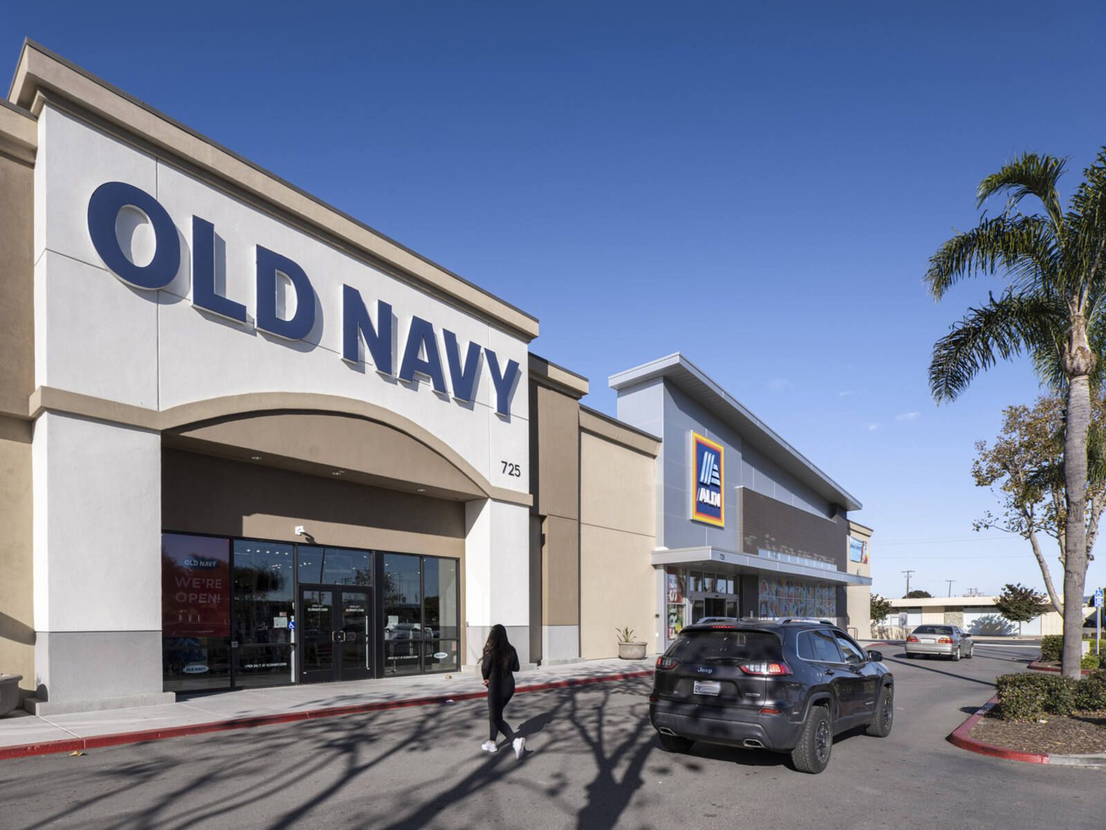 Car and woman in road in front of Old Navy with palm tree on the right.
