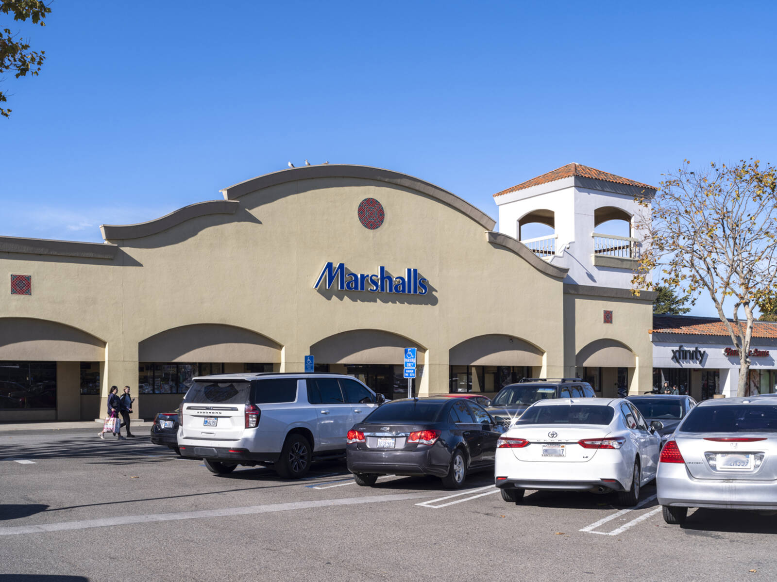 Cars lined up in front of parking lot for Marshalls with two patrons approaching entrance. 