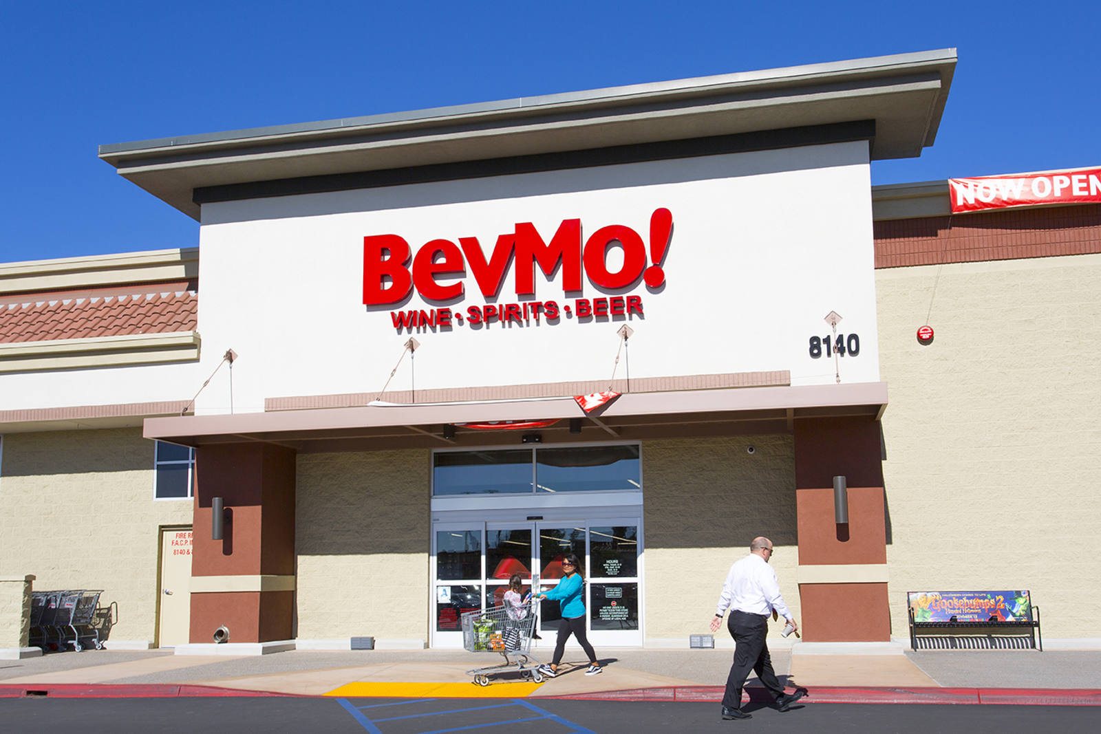 Two people walking otu of BevMo! with a shopping cart on a cloudless day