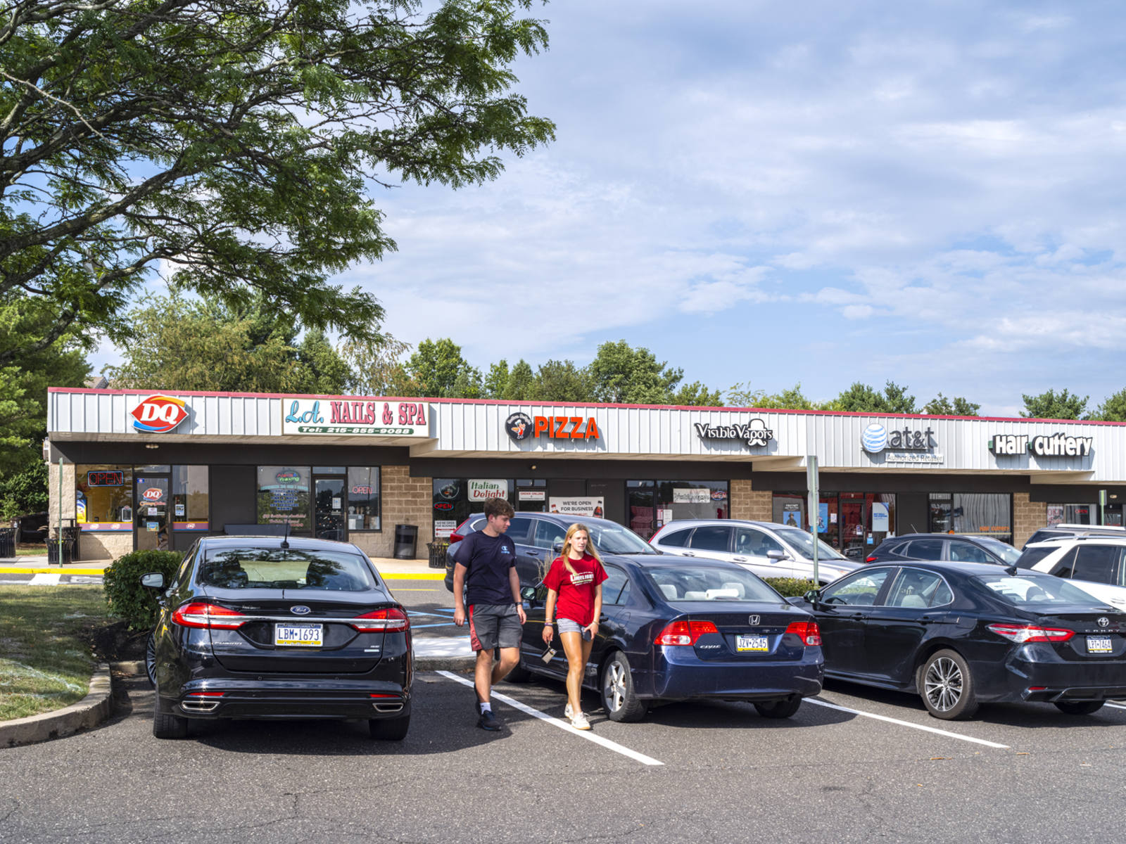 Two young people walking through parked cars at North Penn Market Place shopping center.