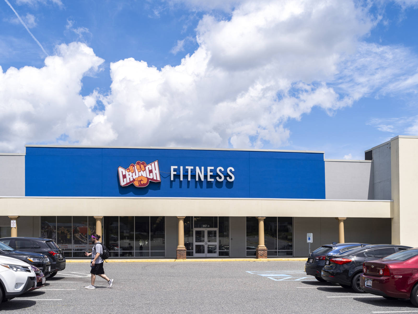Person in black shorts walking towards car in Crunch Fitness parking lot at Perkins Farm Marketplace shopping center