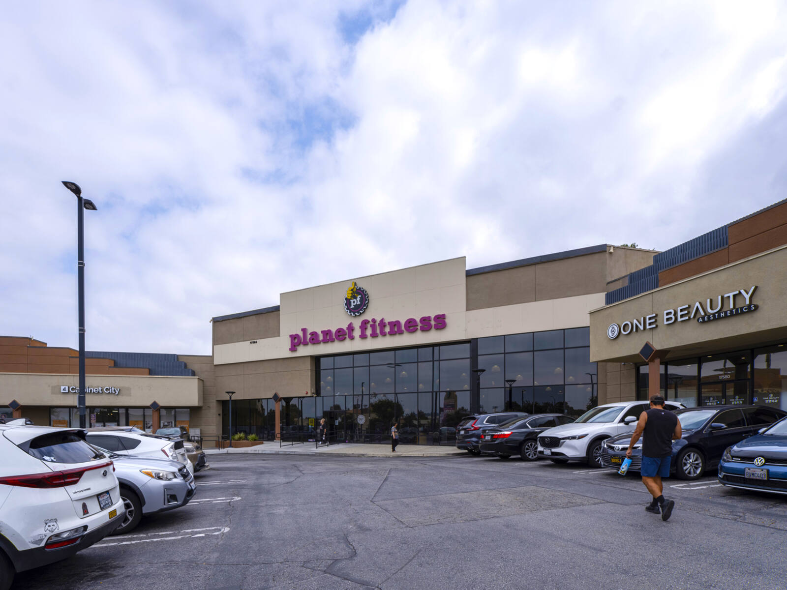 Man approaches Planet Fitness entrance through busy parking lot.