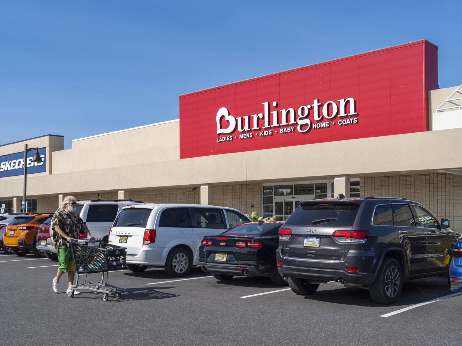 Man with cart passing cars at Burlington parking lot.