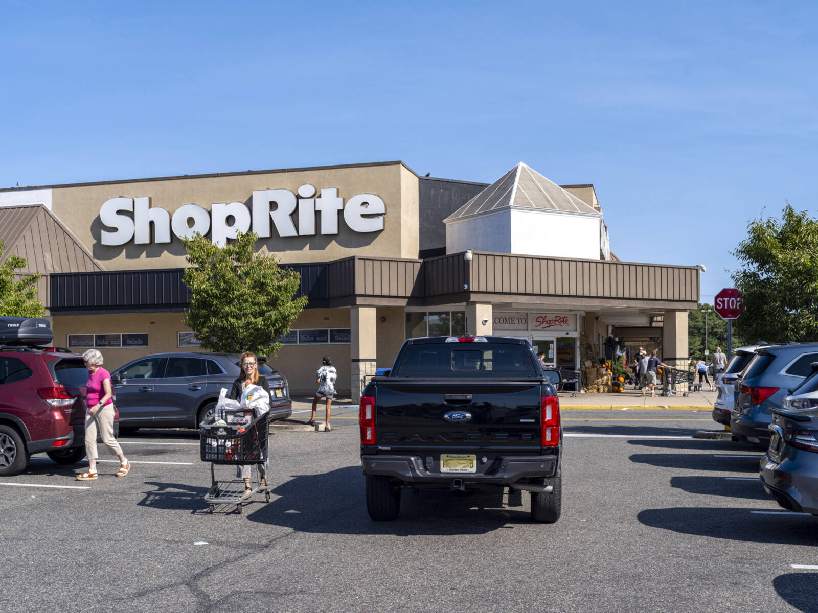 Patron with cart walking up busy parking lot aisle at ShopRite.