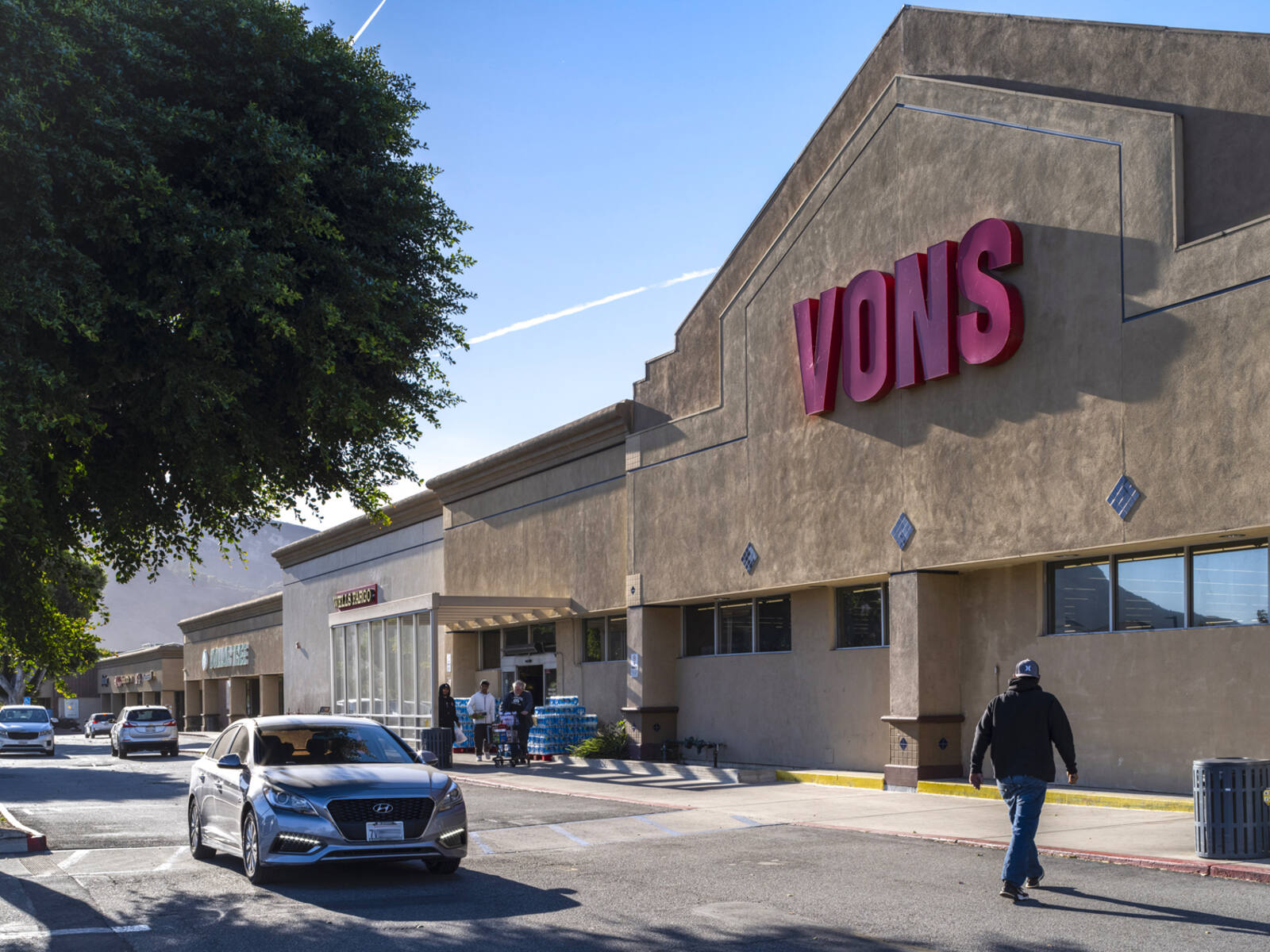 Grey car and man in crosswalk for Vons grocery store.