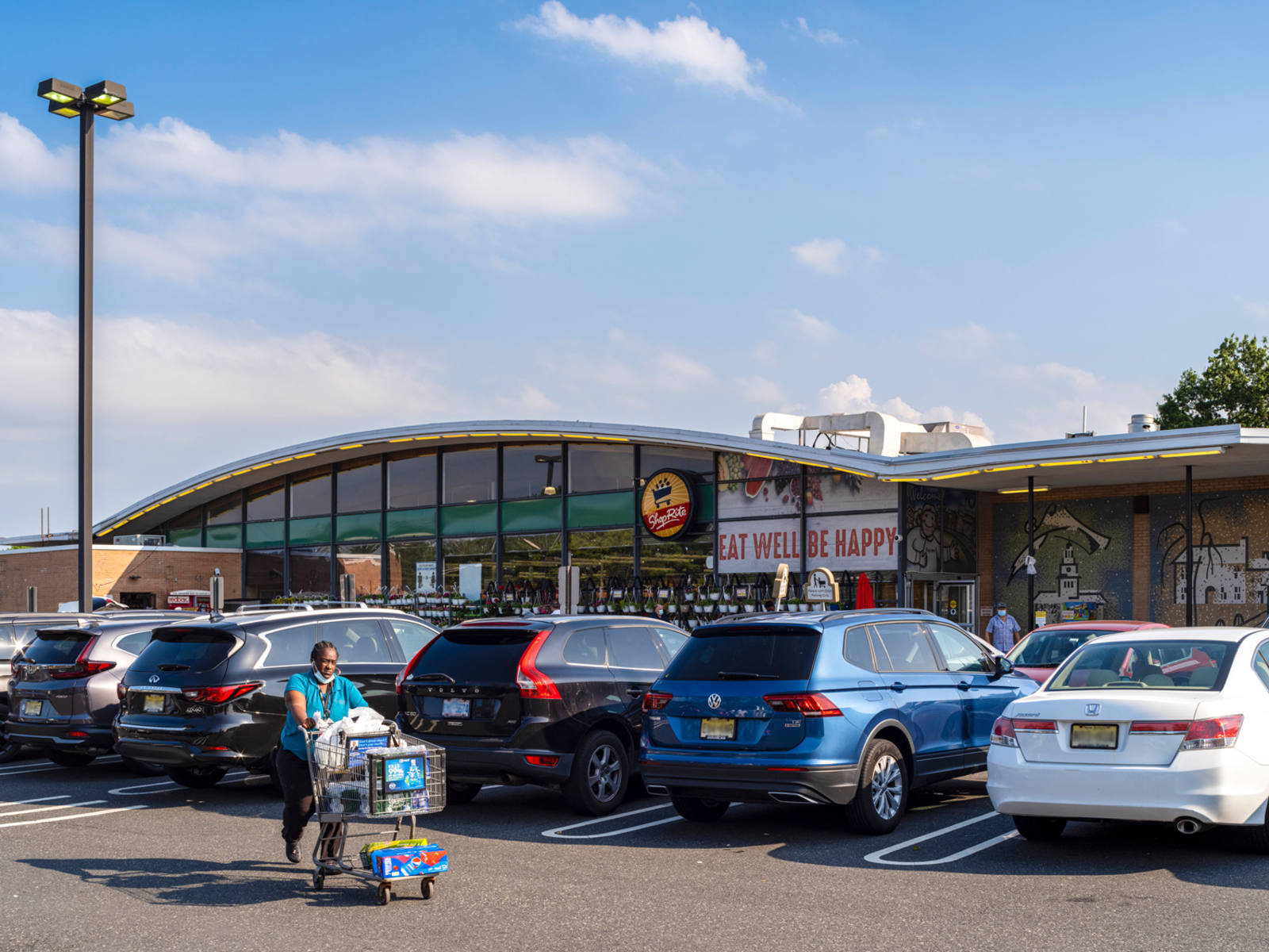 Person with shopping cart walking past parked cars in ShopRite parking lot