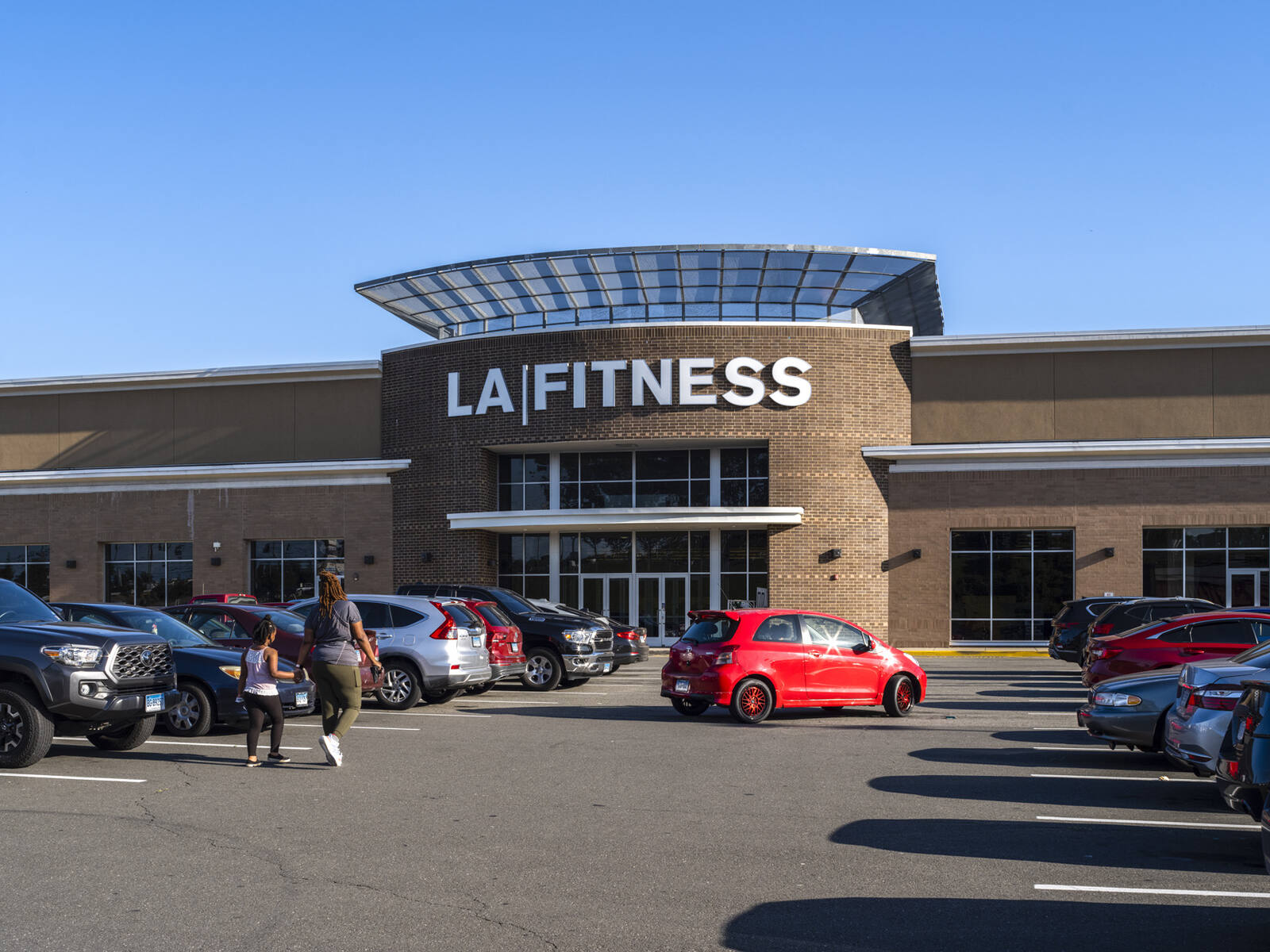 Woman and child walking towards LA Fitness through the parking lot.