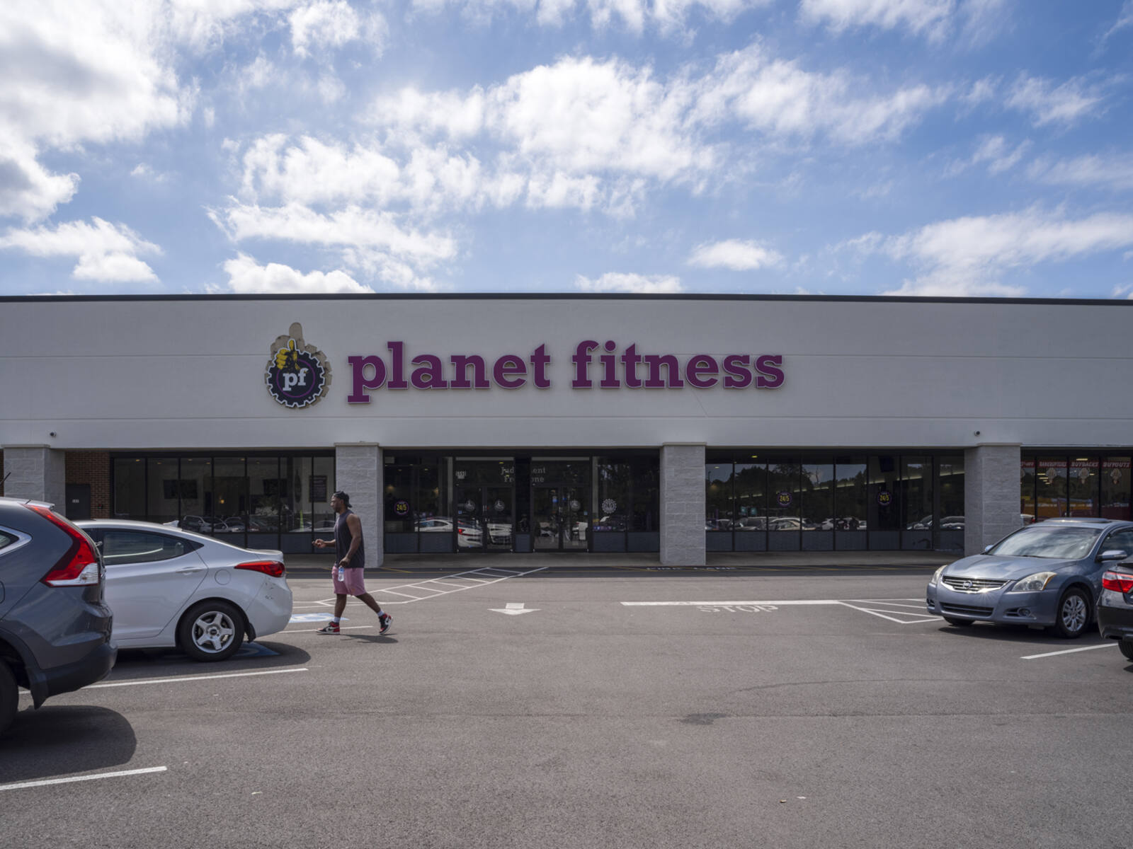 Man approaches silver car in parking lot for Planet Fitness.