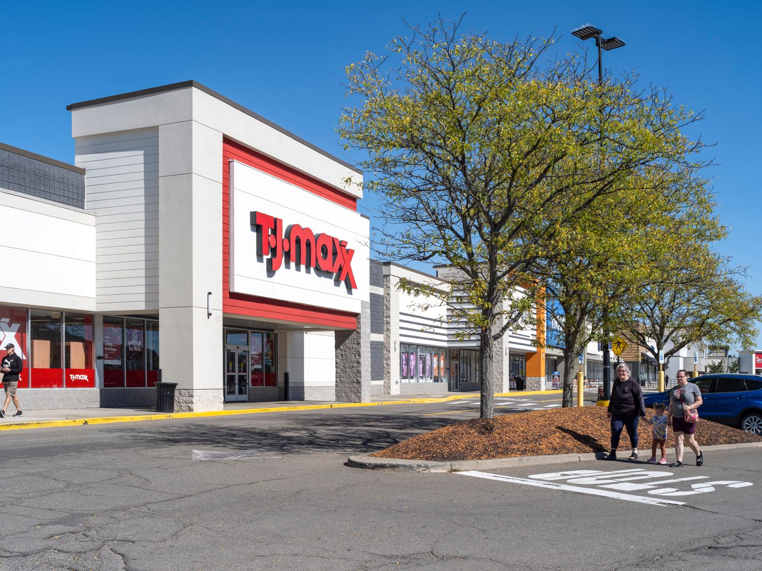 TJ Maxx store with large tree and customers in foreground.