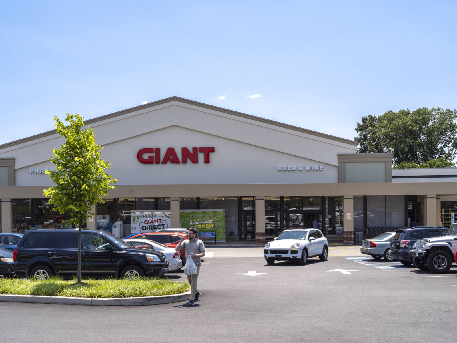 Giant supermarket with trees and cars in front and customer exiting lot.