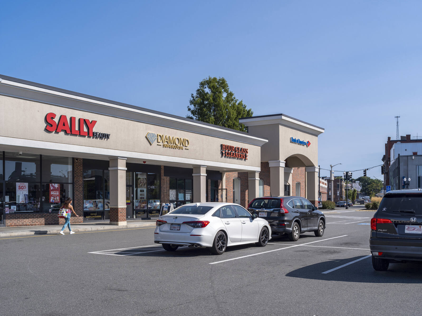 Parking lot and woman on sidewalk in front of Sally Beauty.