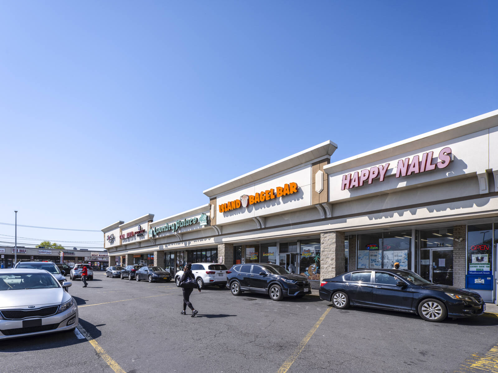 Pedestrians and cars in the lot for Island Bagel Bar and Laundry Palace.