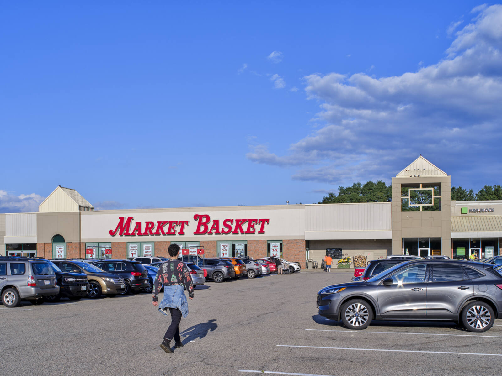Pedestrian walking in parking lot towards Market Basket grocery store.