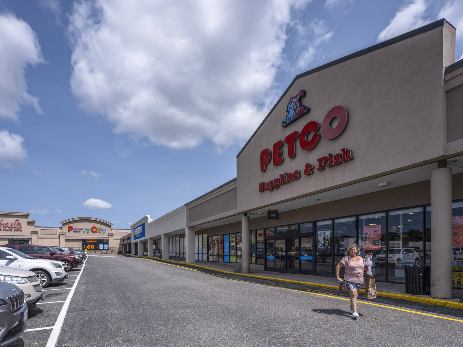 Woman walking along access road in front of Petco with Party City in the background.