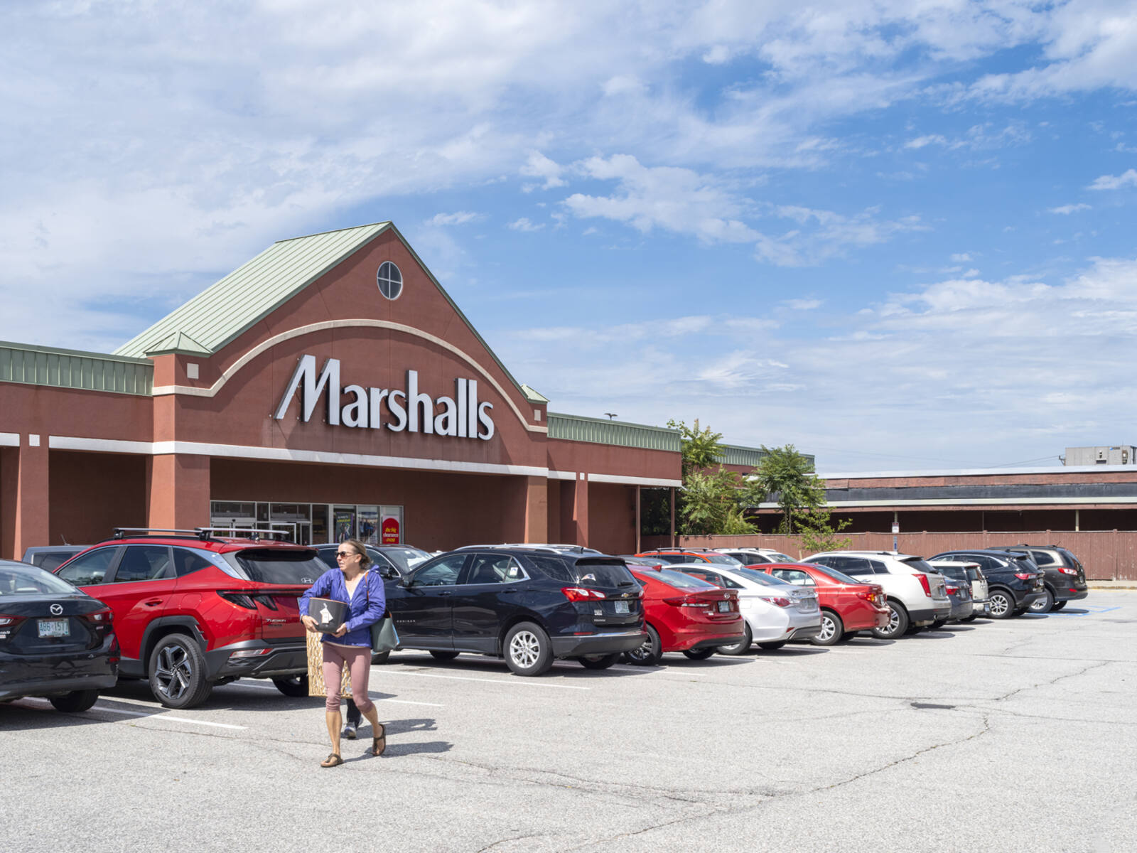 Woman with supplies walking past Marshalls parking lot.