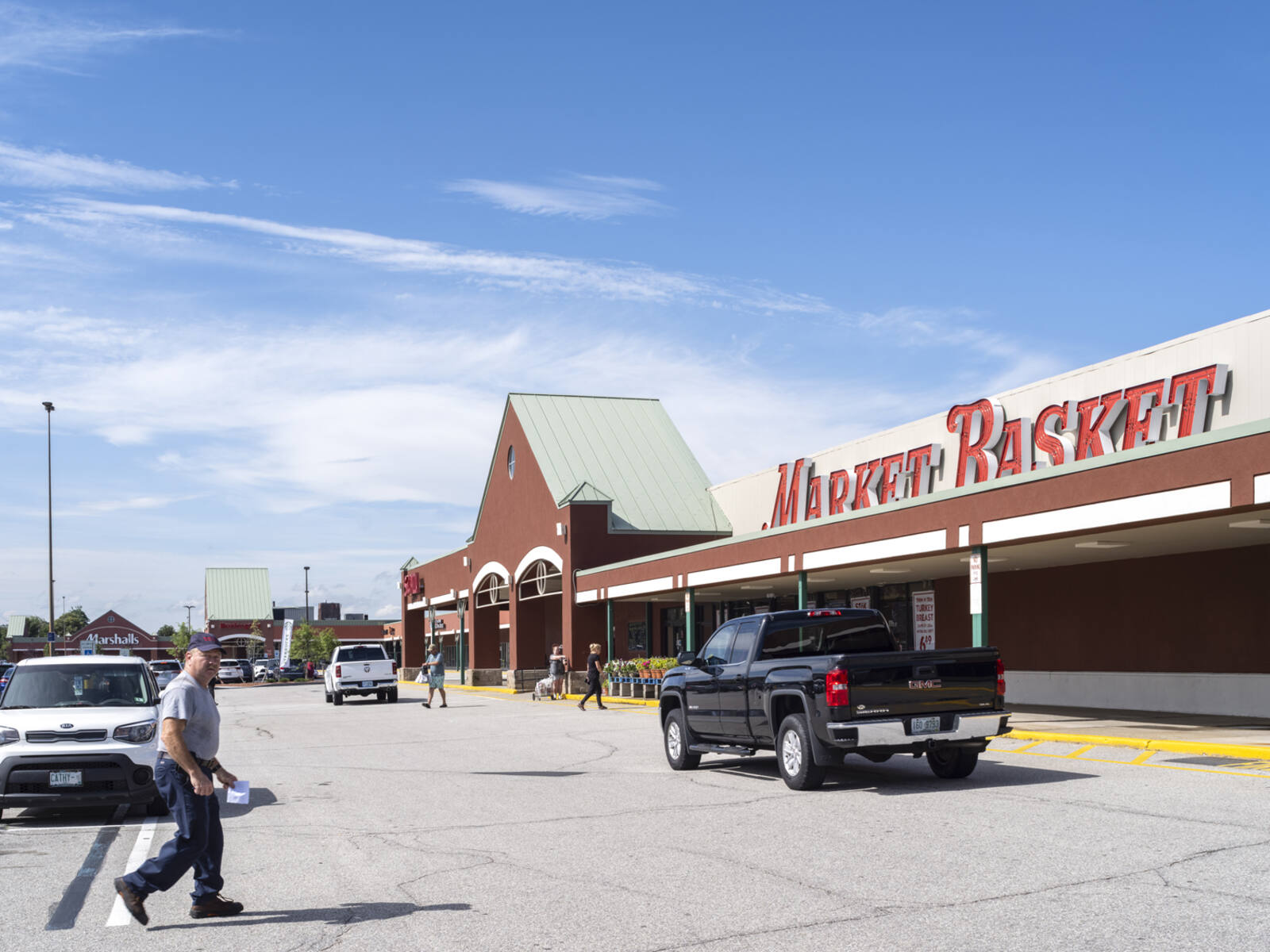 Man in crosswalk of Market Basket with many cars on road.