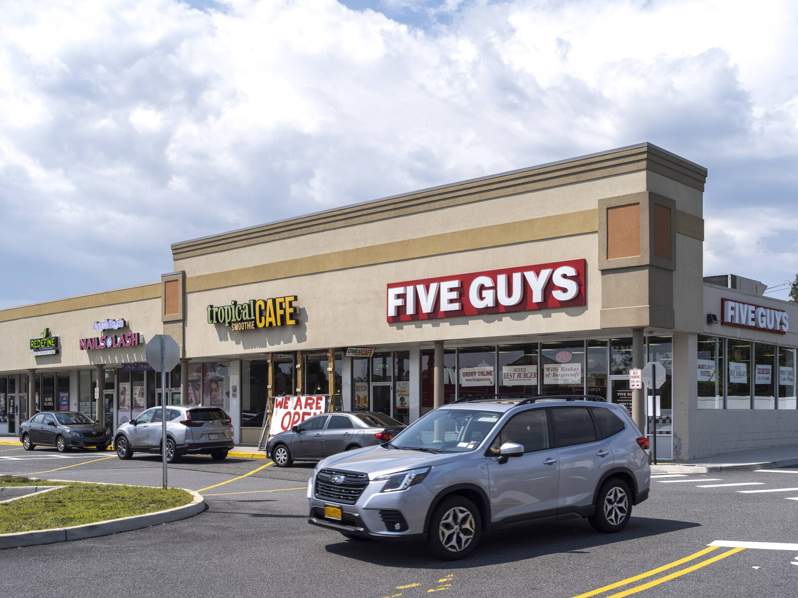 Grey SUV pulls out of parking lot in front of Five Guys burgers.