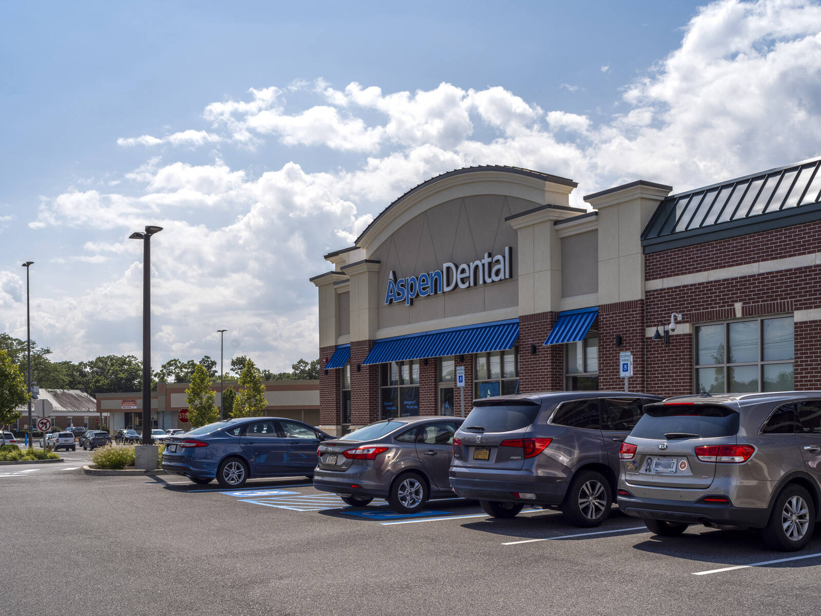 Busy parking lot at Aspen Dental with trees behind it.