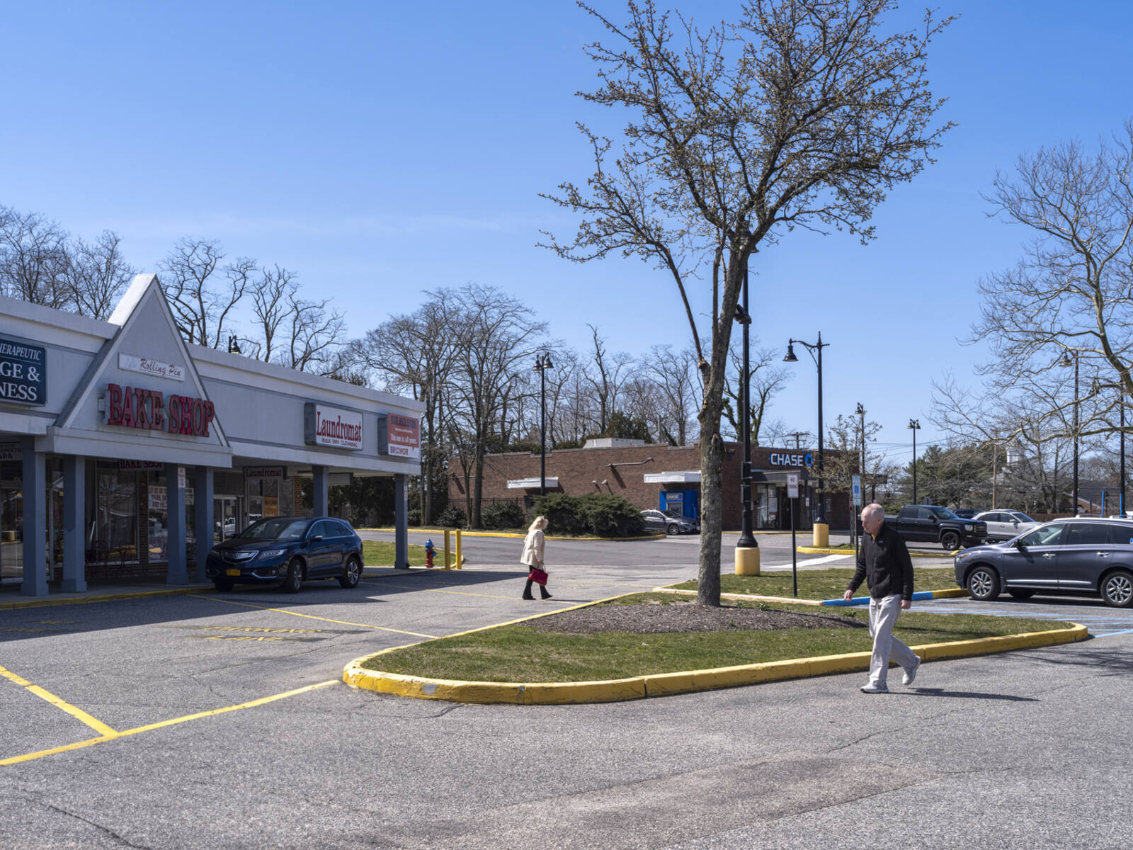 Pedestrians on sides of a planter in front of shopping center parking lot.
