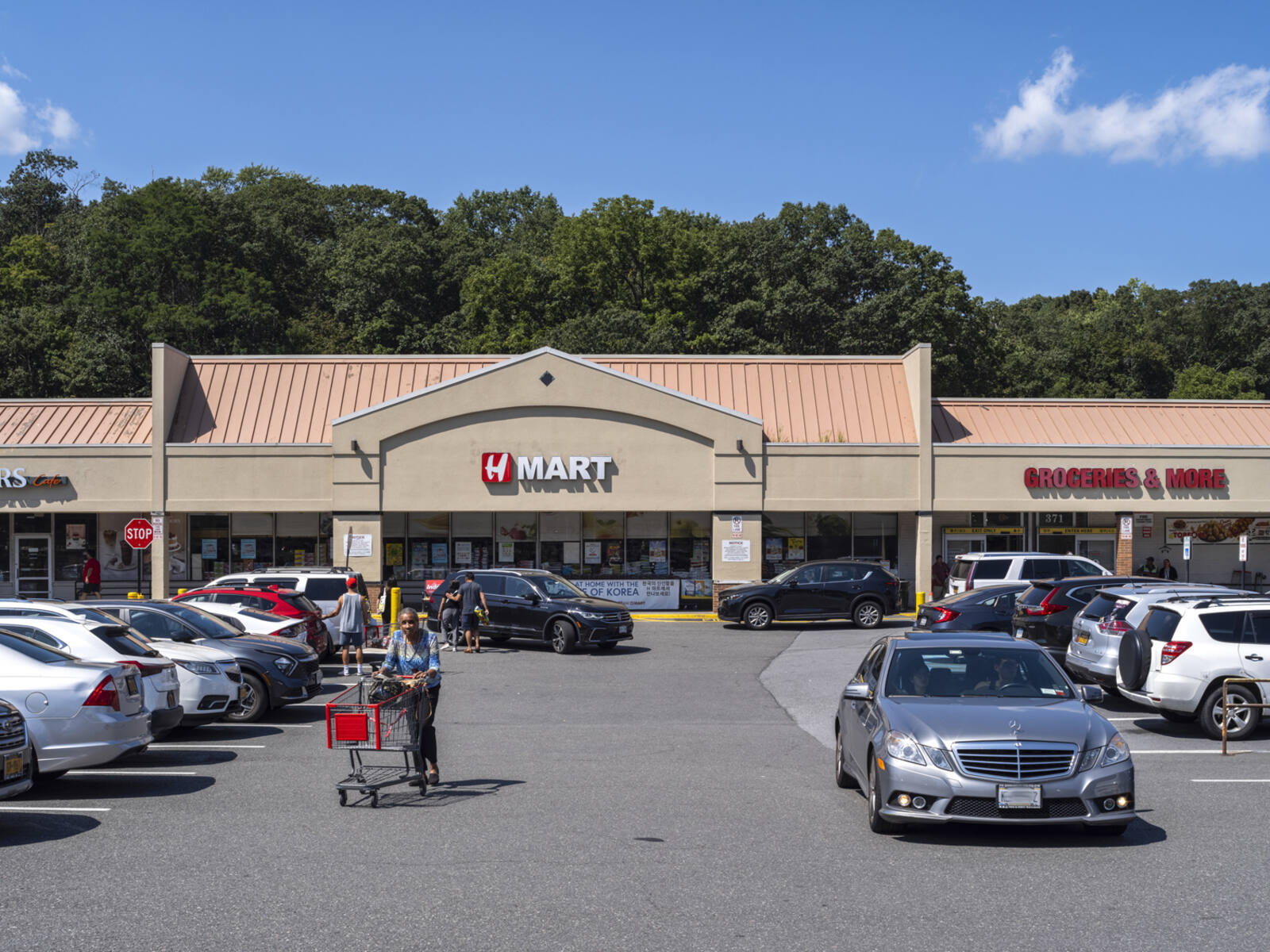Busy parking lot in front of Hmart with customer pushing cart by the side of silver car.
