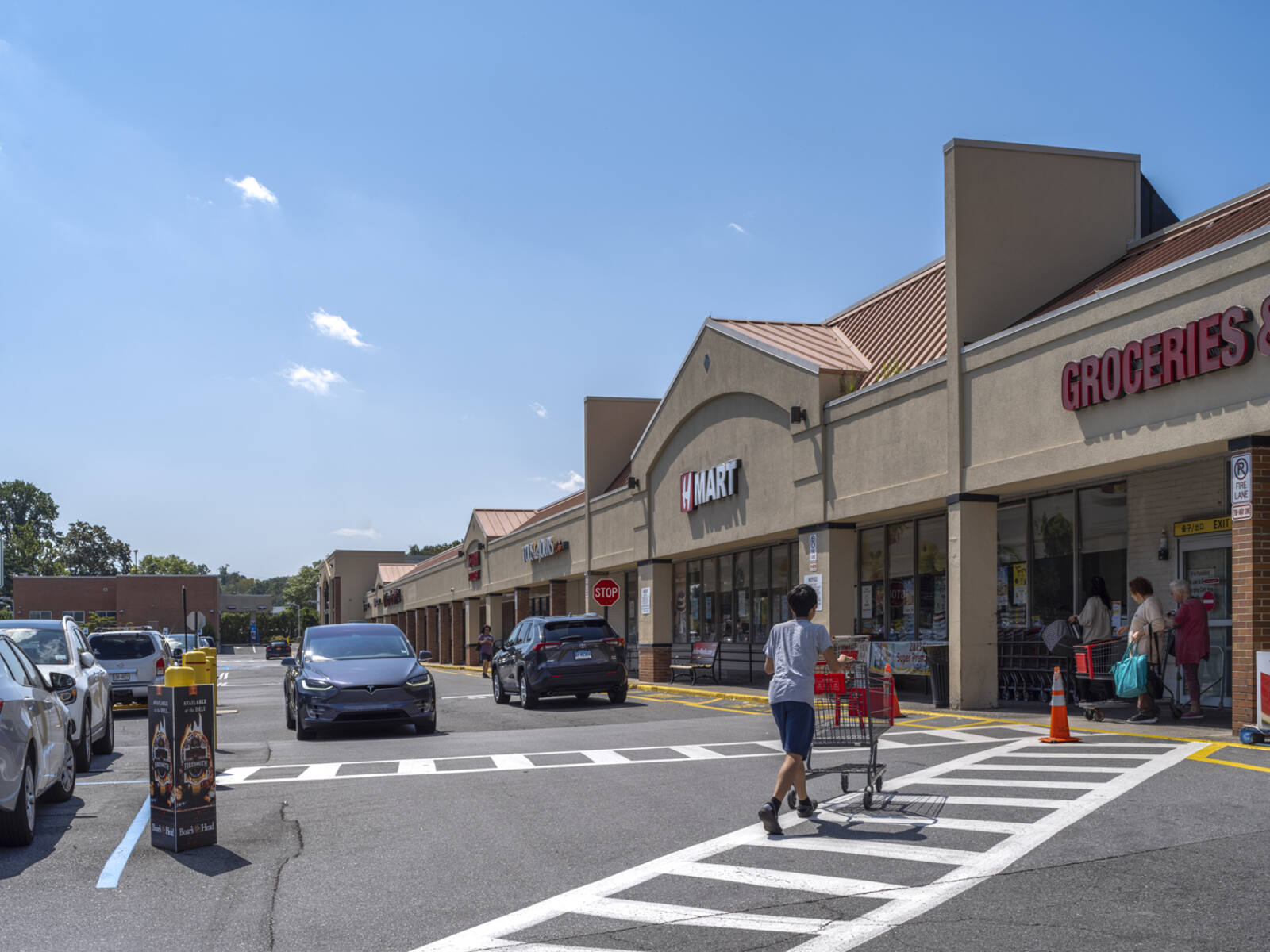 Man with cart in crosswalk to Hmart grocery store with cars passing in front of him.