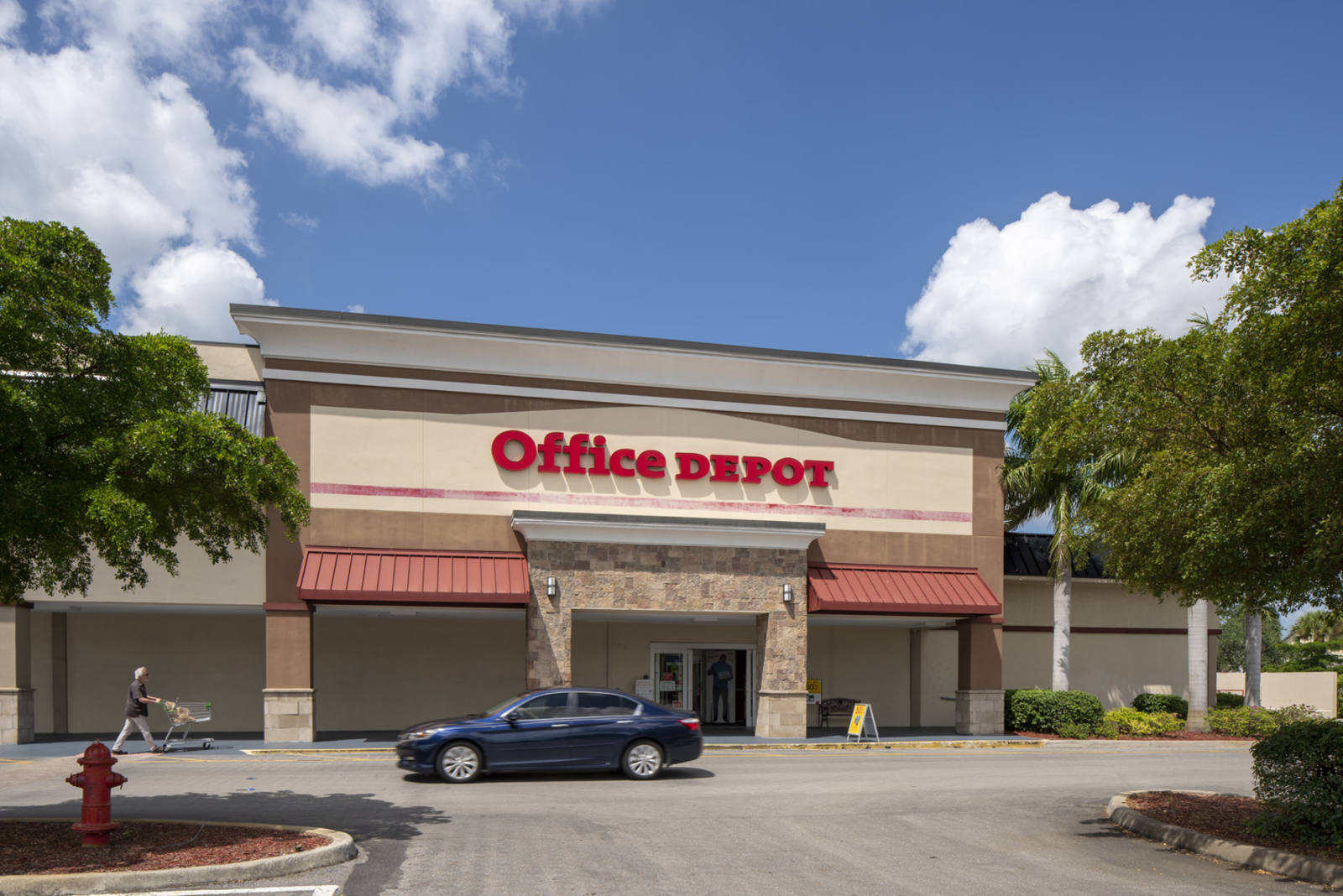 Office Depot with blue car and trees in front at Naples Plaza.