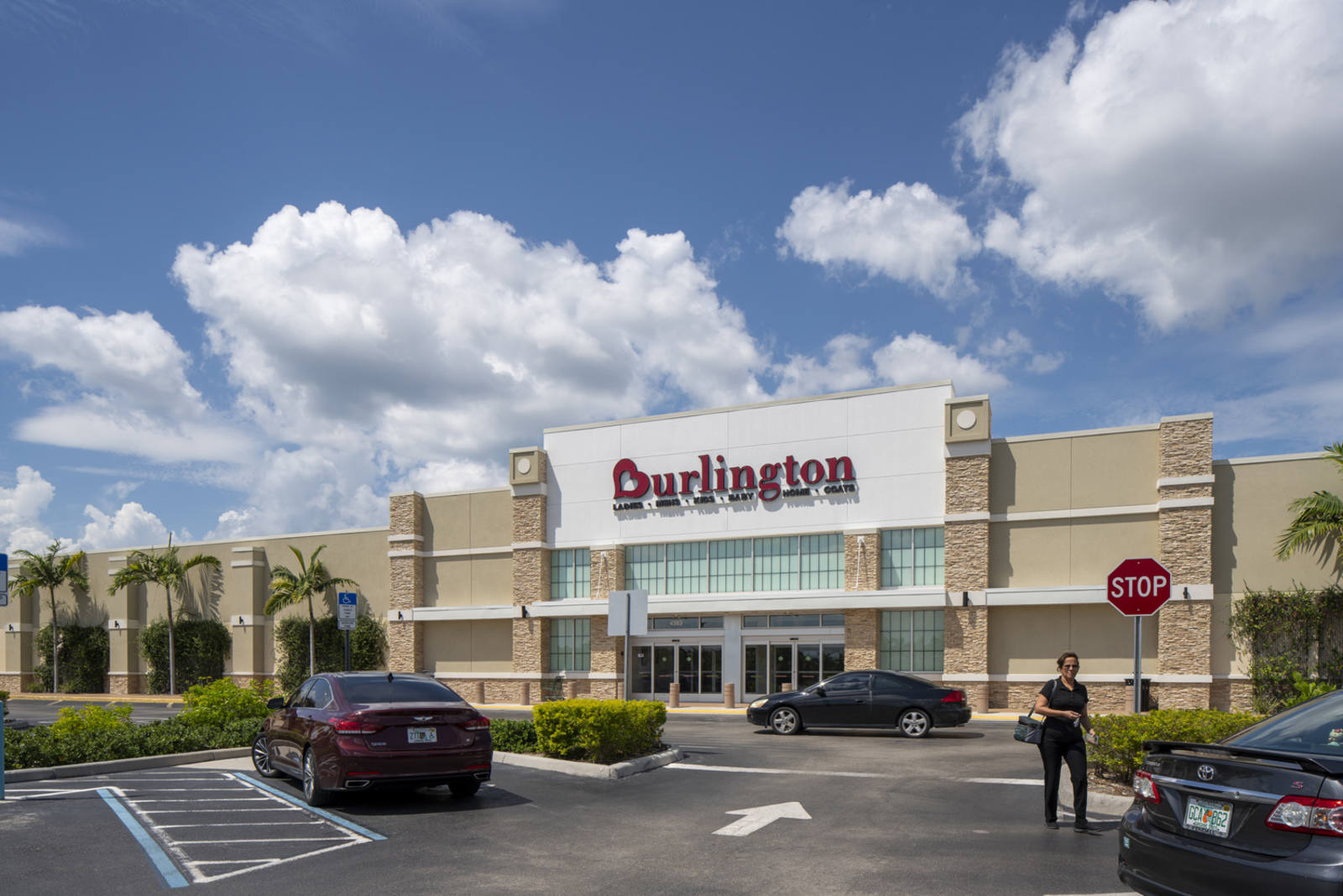 Person in black walking towards car in parking lot in front of Burlington on a sunny day