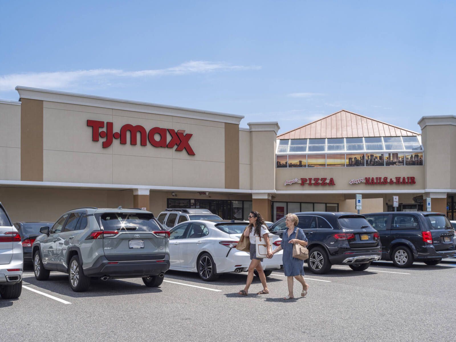Two women passing row of cars in TJ Maxx parking lot.