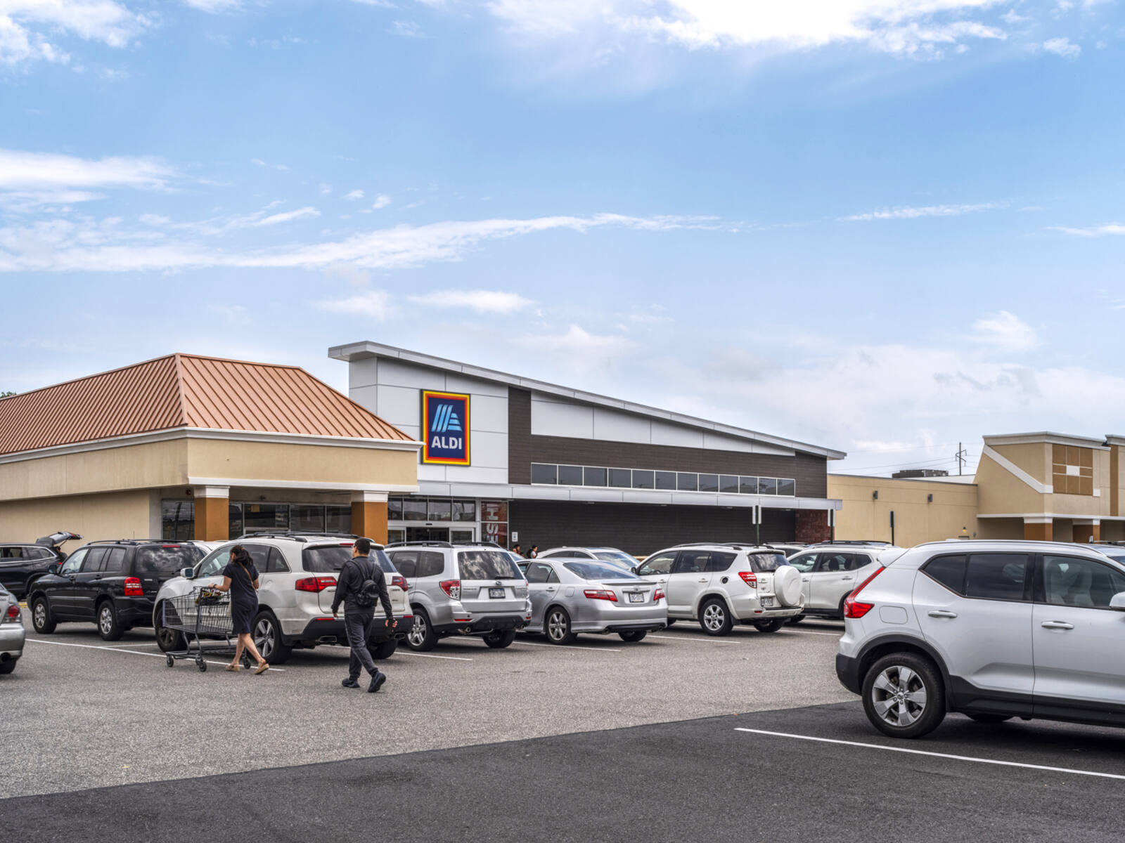 Aldi with customers pushing carts in busy parking lot.