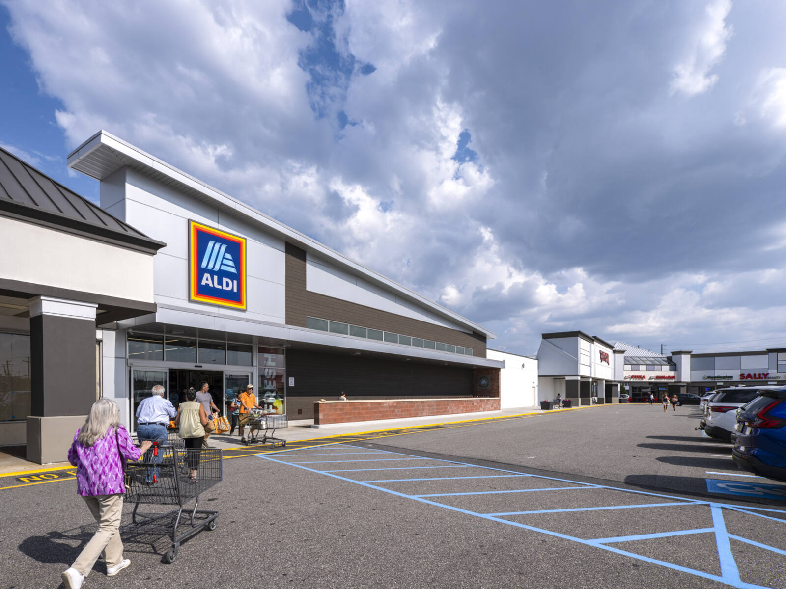 Customers with cars approach Aldi entrance with grey cloudy sky above.
