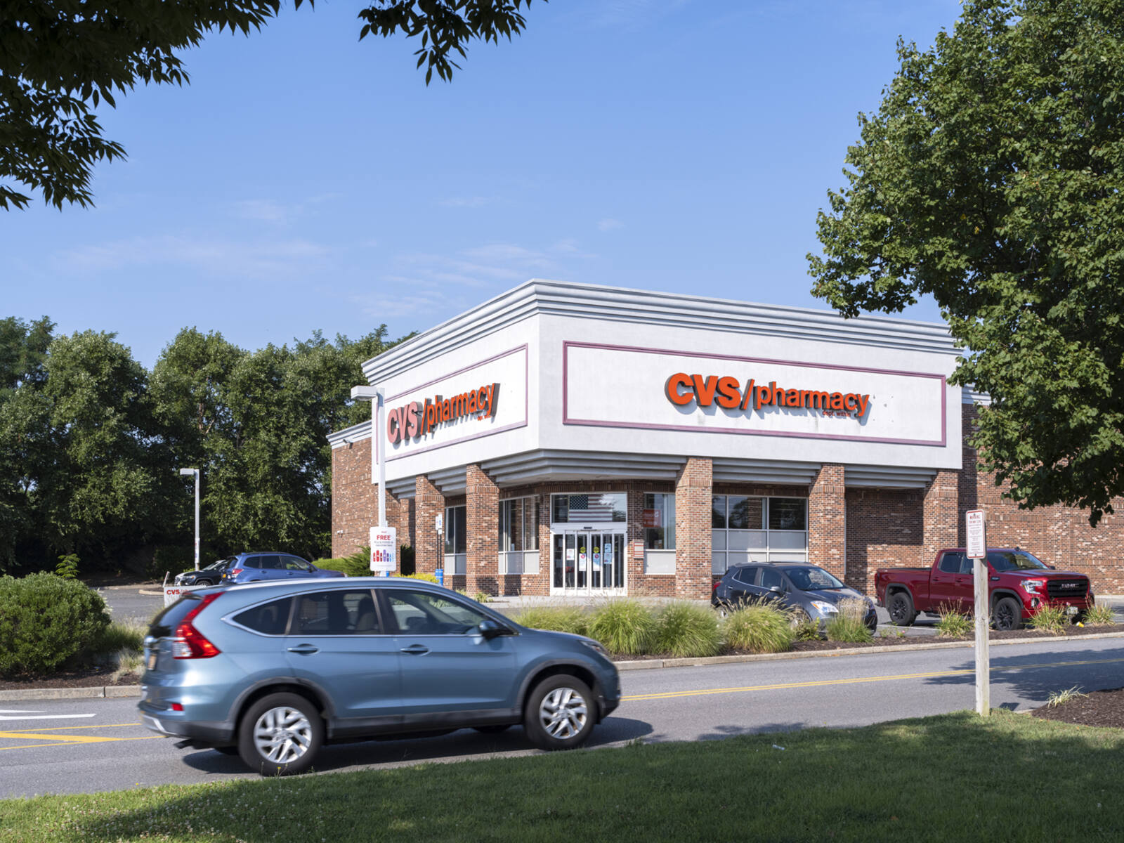 Blue SUV passing CVS Pharmacy with trees and bushes.