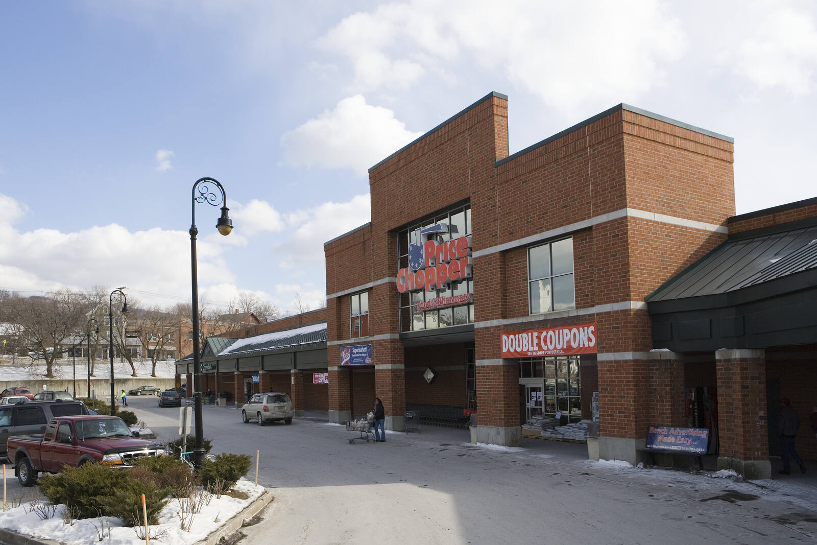 Person with shopping cart walking through parking lot of Price Chopper with snow on the ground
