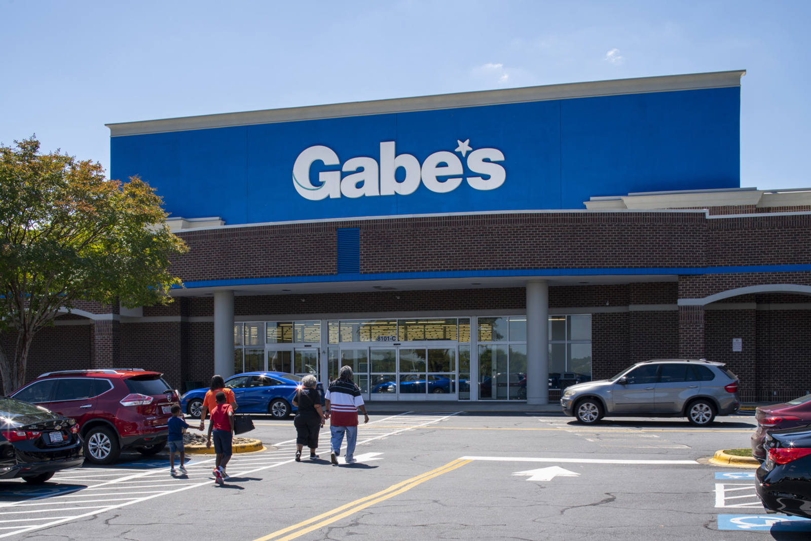 Four people walking towards Gabe's and cars passing in front