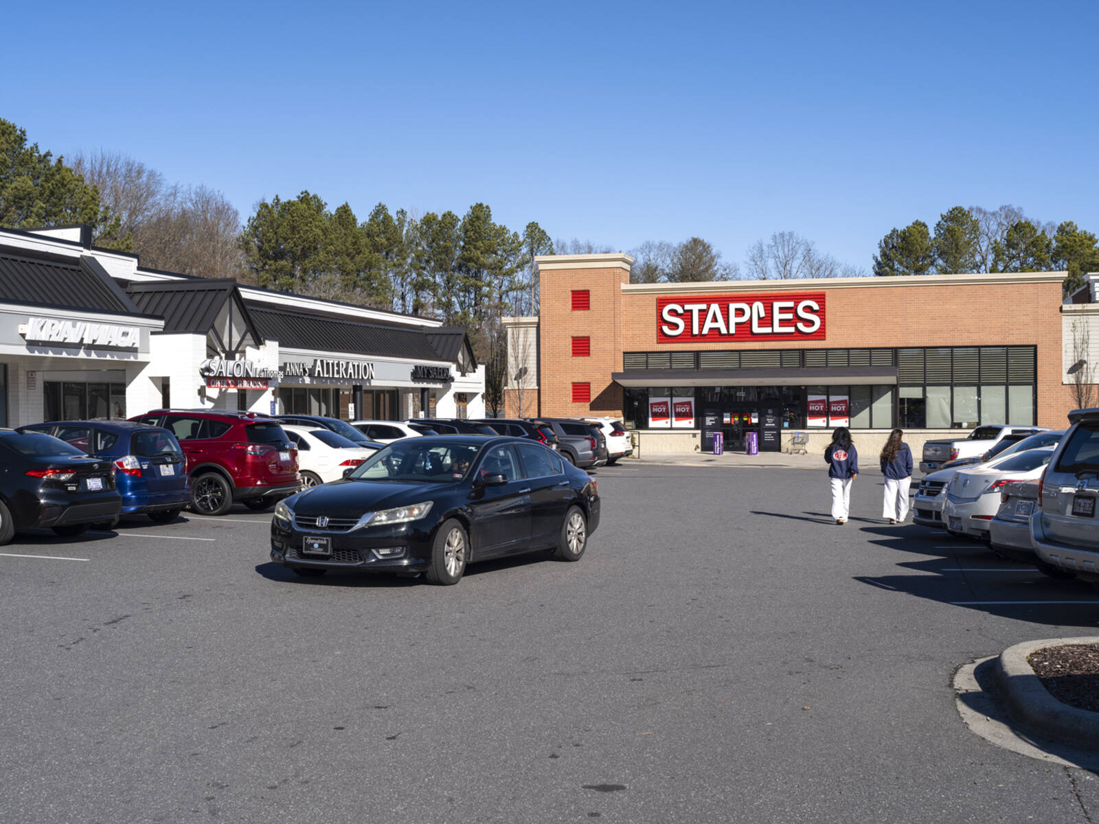 Black car passes up parking aisle in front of Staples.
