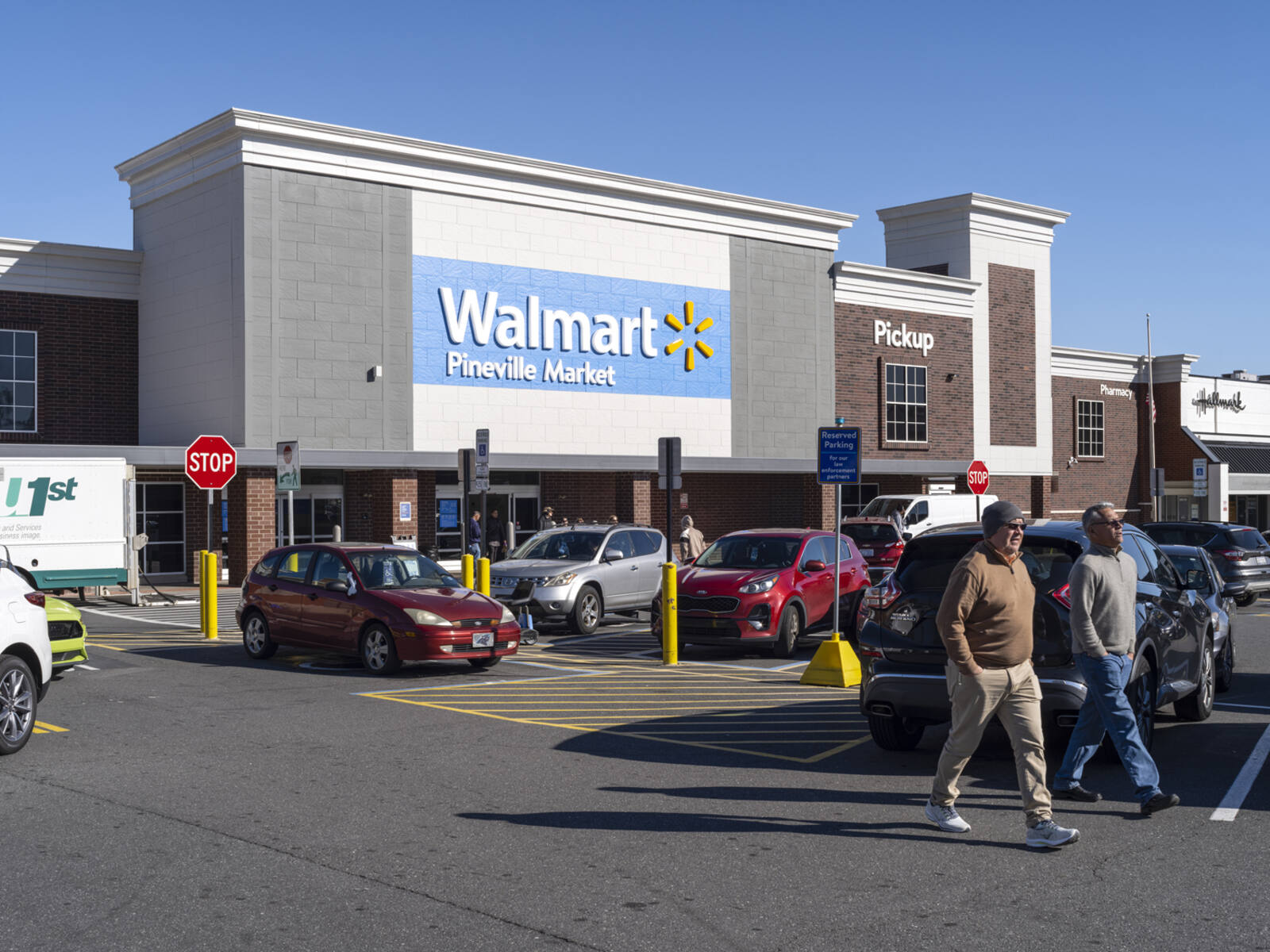 Two men leaving Walmart parking lot with many cars and Walmart entrance behind them.