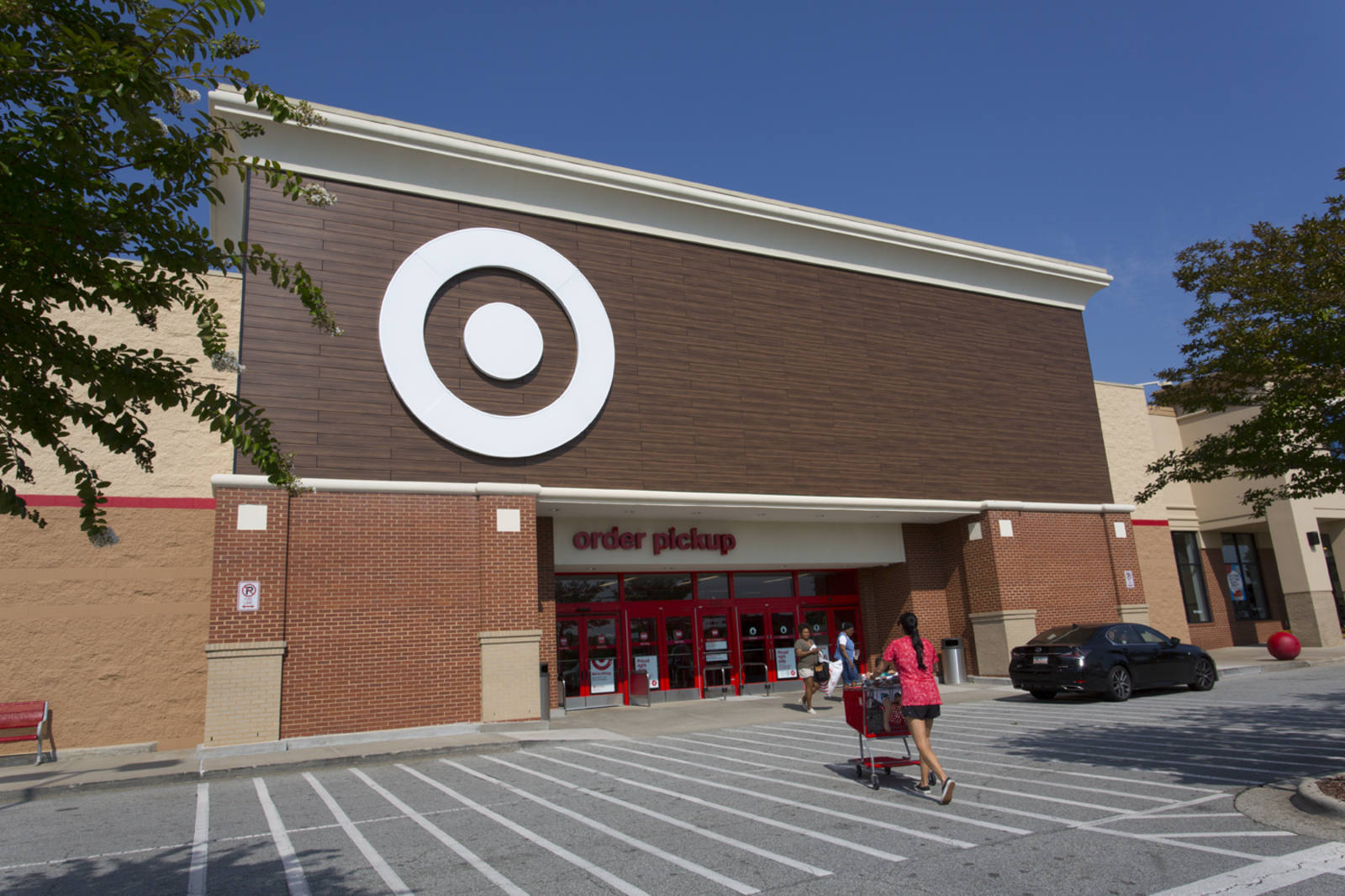 Woman in red shirt and black shorts walking into a Target with a shopping cart