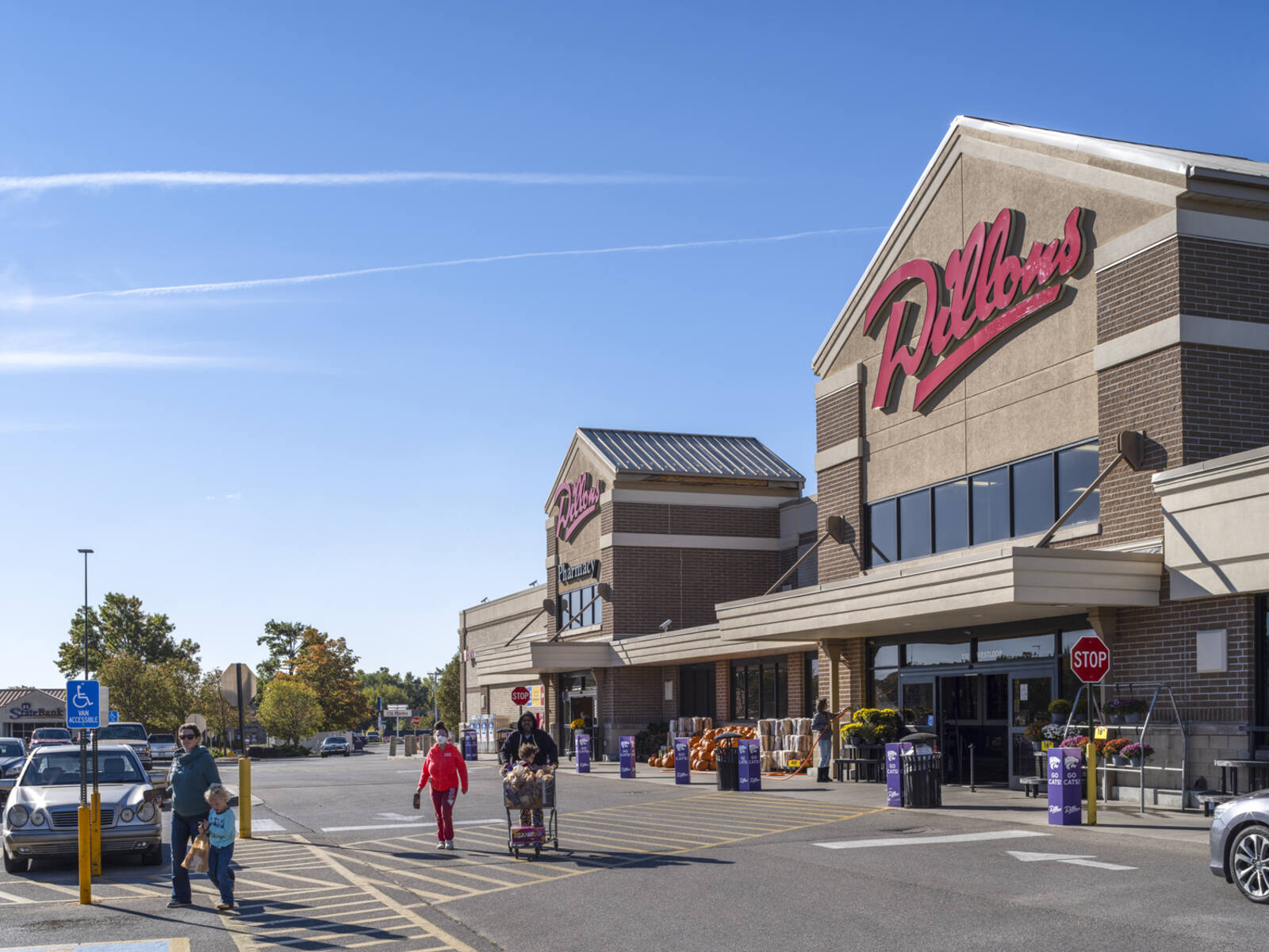 Shoppers with children and carts exit Dillons supermarket into the parking lot.