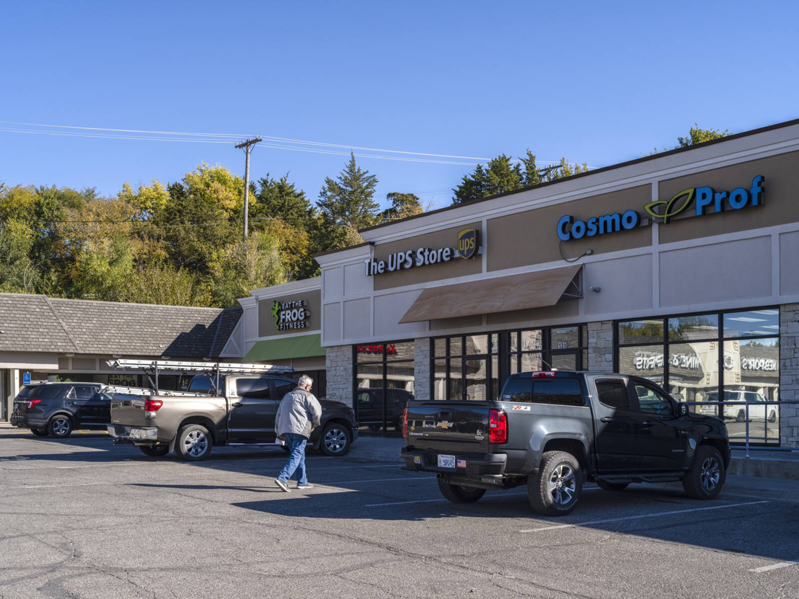 Man walking towards UPS Store past a grey jeep in a parking lot.